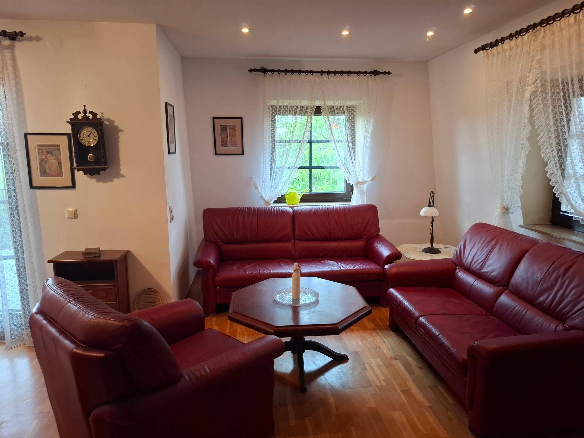 Gemütliches Wohnzimmer mit roten Ledersofas, Holzboden und einem Fenster mit Vorhängen.