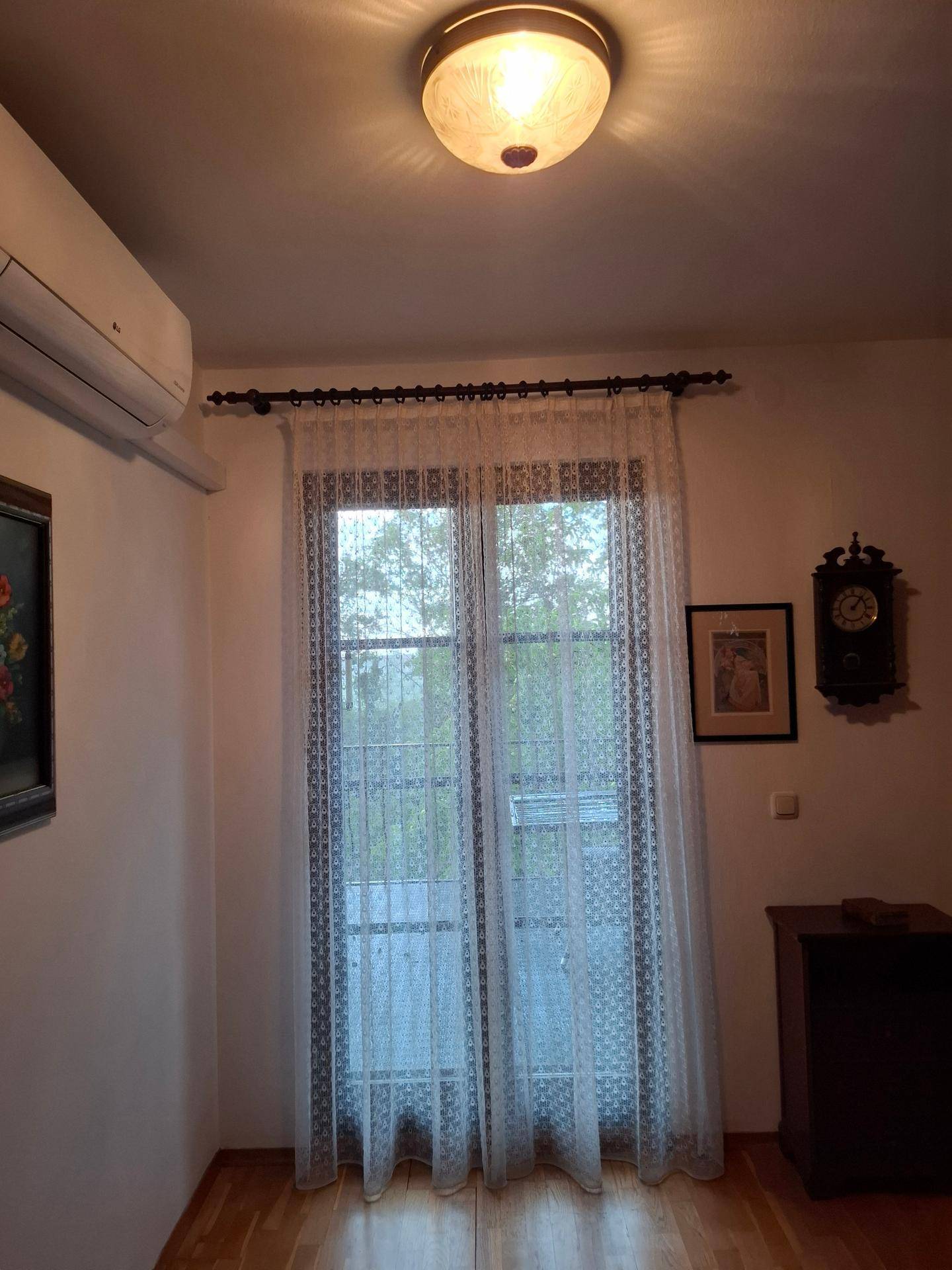 Fenstertür mit weißen Spitzenvorhängen und einer Klimaanlage an der Wand.