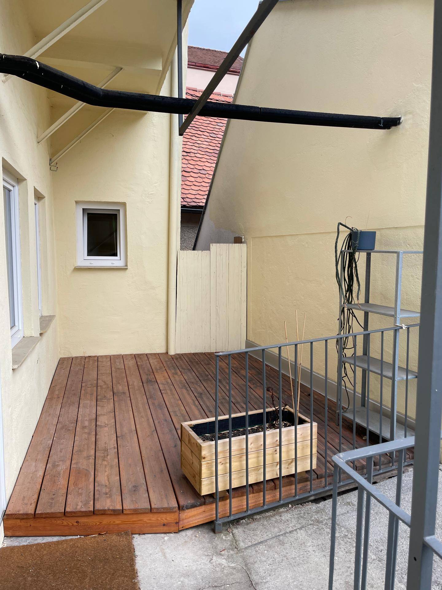 Kleine Holzterrasse im Hinterhof mit einem Blumenkasten und schlichtem Metallgeländer.