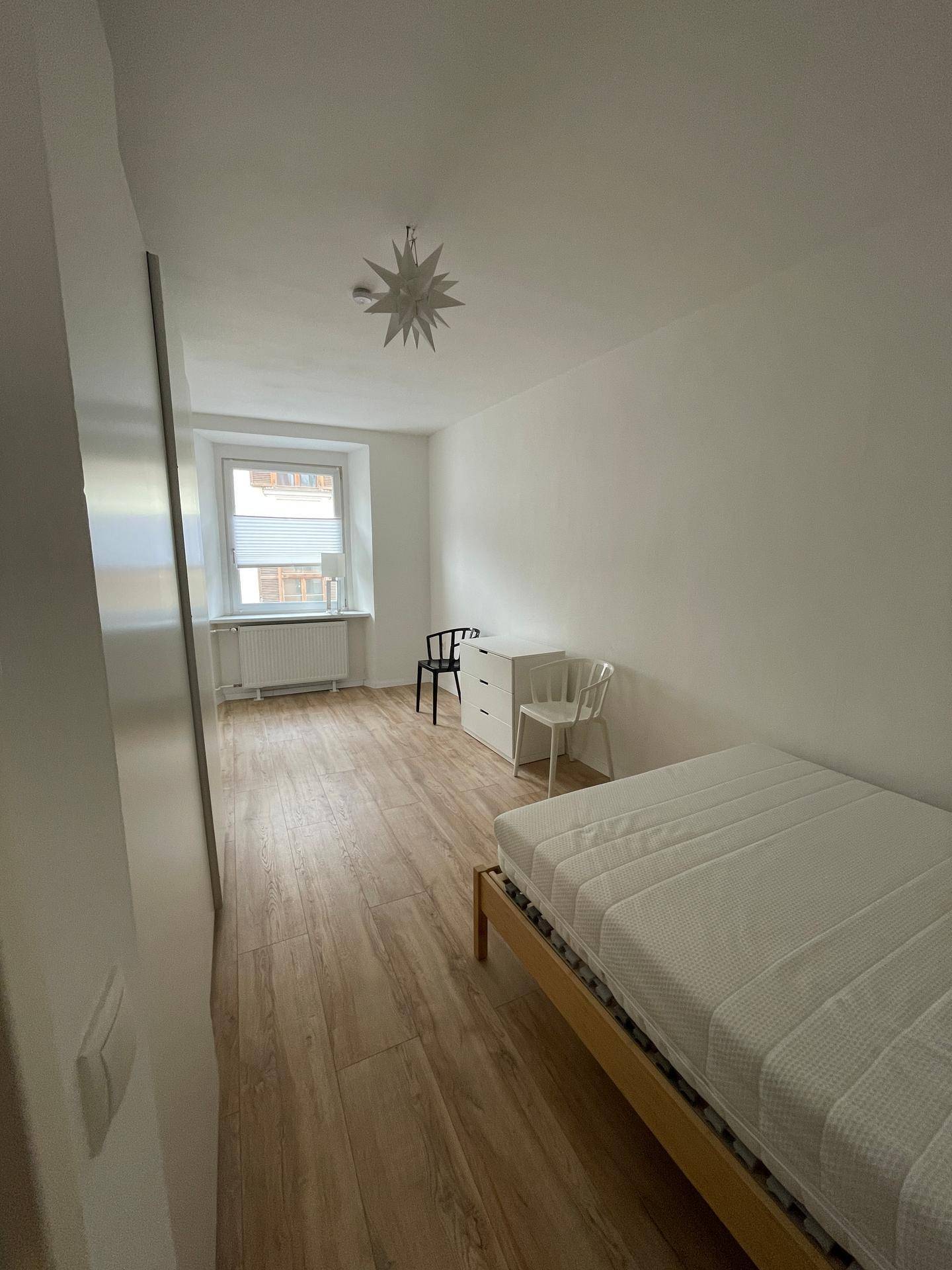 Helles Schlafzimmer mit Holzbett, Kommode und Fenster, ausgestattet mit Holzfußboden.
