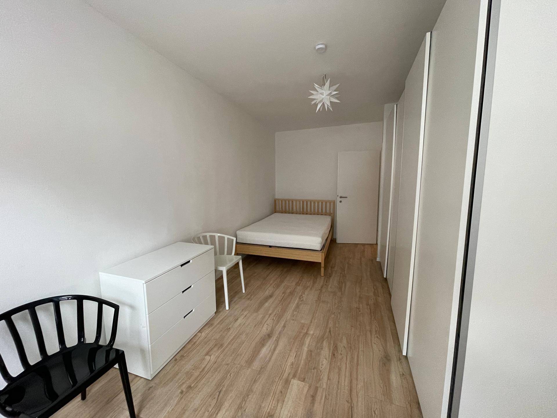 Geräumiges Schlafzimmer mit Holzbett, Kommode und großen weißen Schränken, auf hellem Holzfußboden.