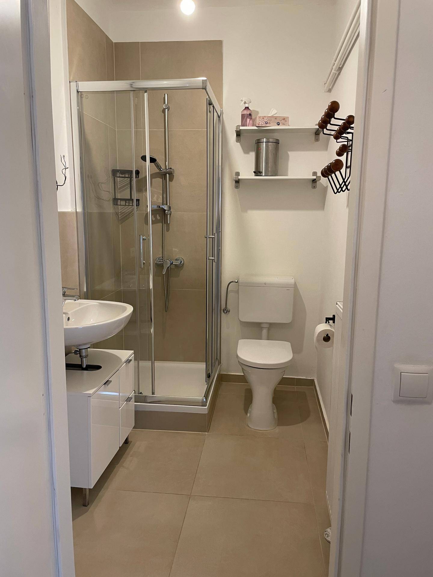 Helles Badezimmer mit Duschkabine, Waschbecken und WC, ausgestattet mit beigen Fliesen.