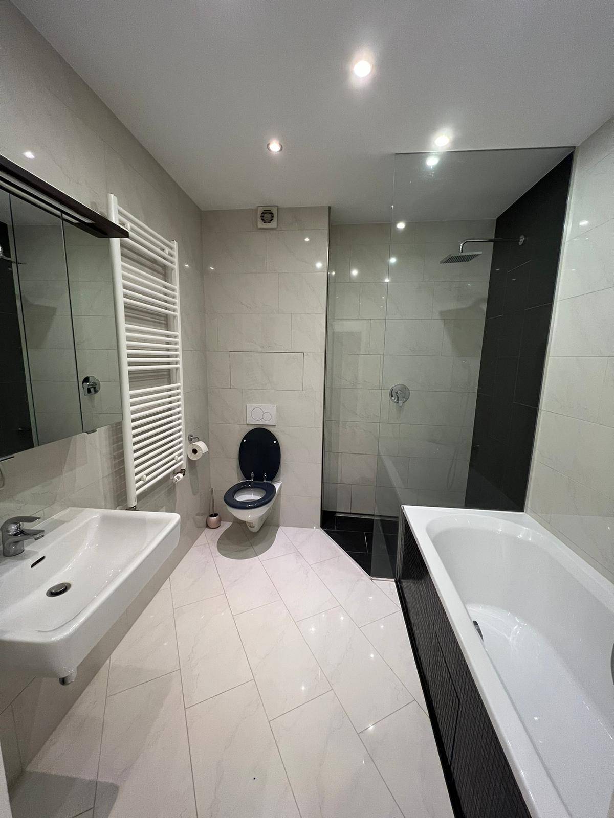 Modernes Badezimmer mit weißen Fliesen, Dusche, Badewanne und beheiztem Handtuchhalter.