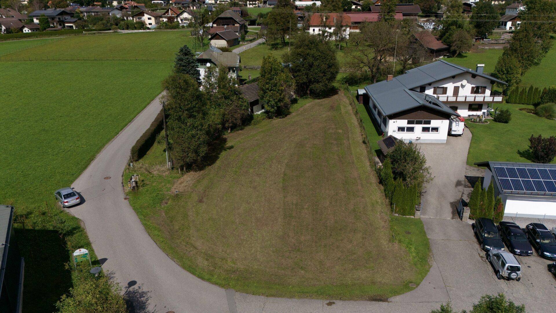 Luftbild eines unbebauten Grundstücks umgeben von Wohnhäusern und grüner Landschaft mit Weitblick.