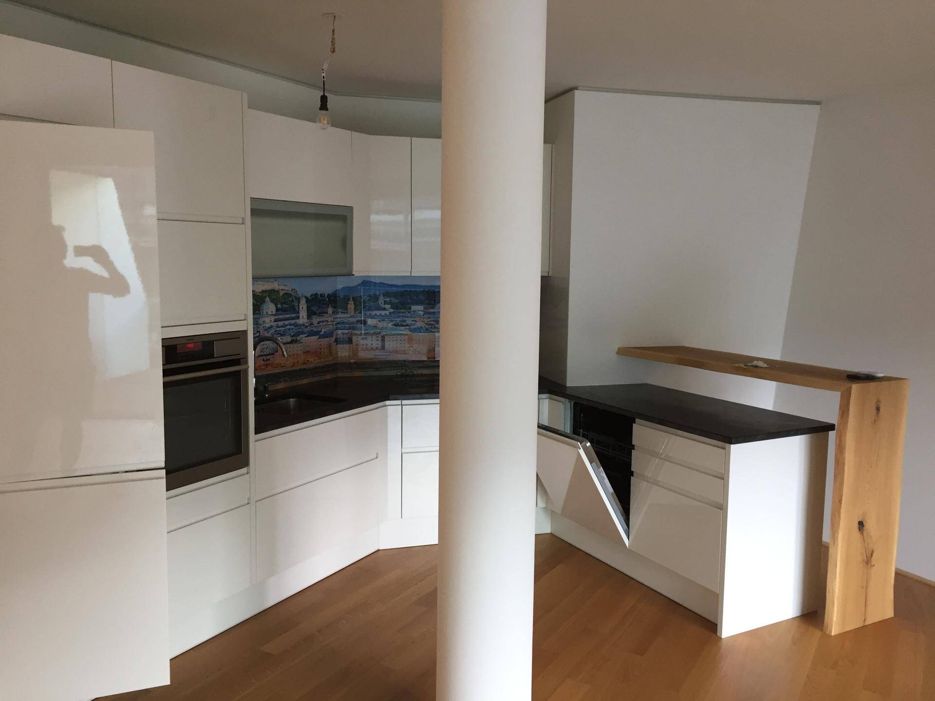Moderne Küche mit weißen Hochglanzfronten, integrierten Geräten und einer Frühstücksbar aus Holz.