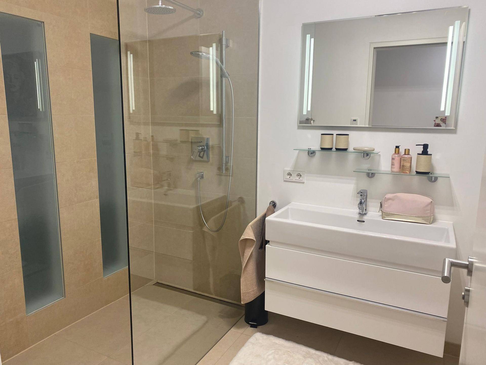 Modernes Badezimmer mit ebenerdiger Dusche, Einzelwaschbecken und beleuchtetem Spiegelschrank.