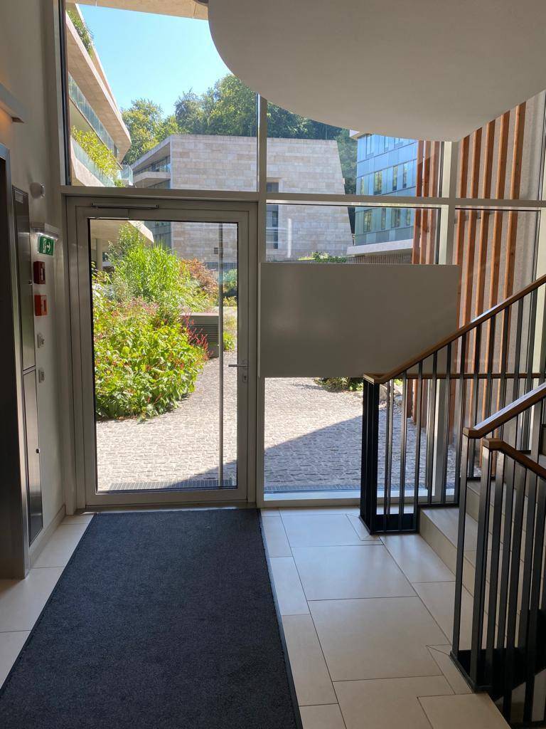 Heller Eingangsbereich mit Glasfront zum begrünten Innenhof, Treppe und Aufzug.