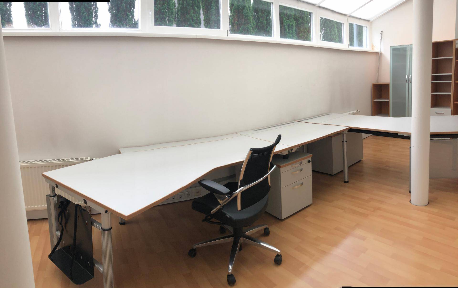 Heller Arbeitsbereich mit mehreren Schreibtischen und ergonomischen Bürostühlen unter einem Glasdach.