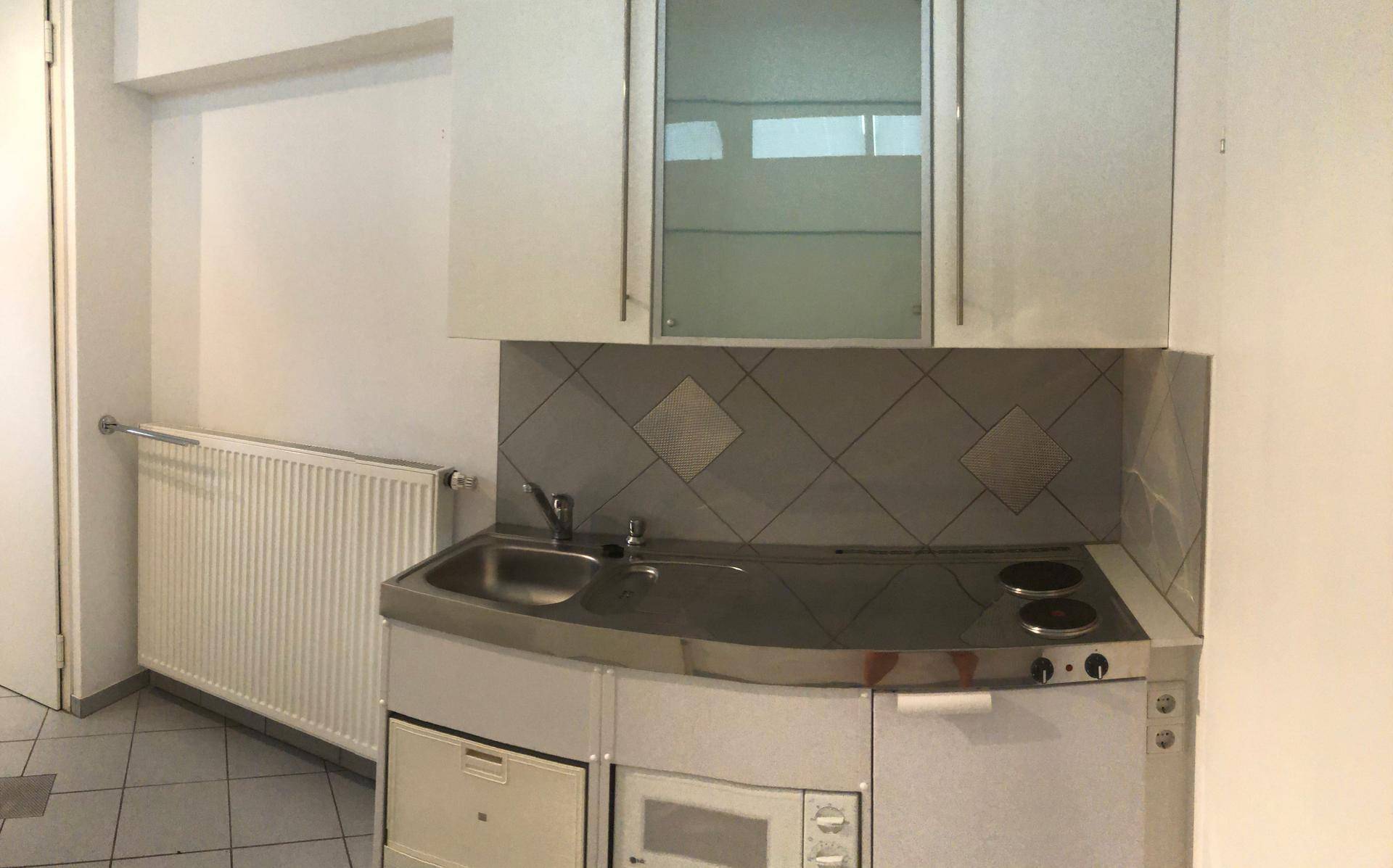 Kompakte Küchenzeile mit Spüle, Kochplatten und Mikrowelle, ideal für kleine Wohnungen oder Büros.