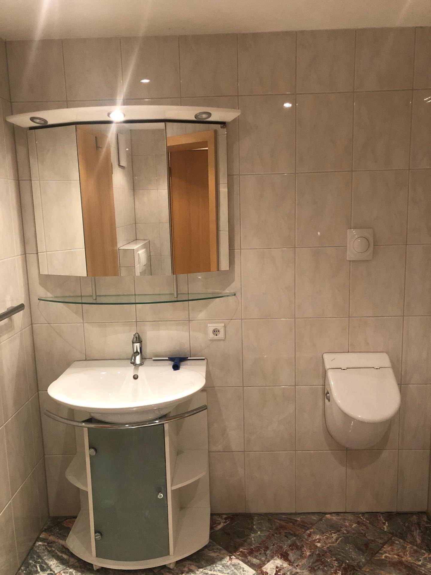 Badezimmer mit Waschtisch, Spiegelschrank und Wand-WC, ausgestattet mit hellen Fliesen.