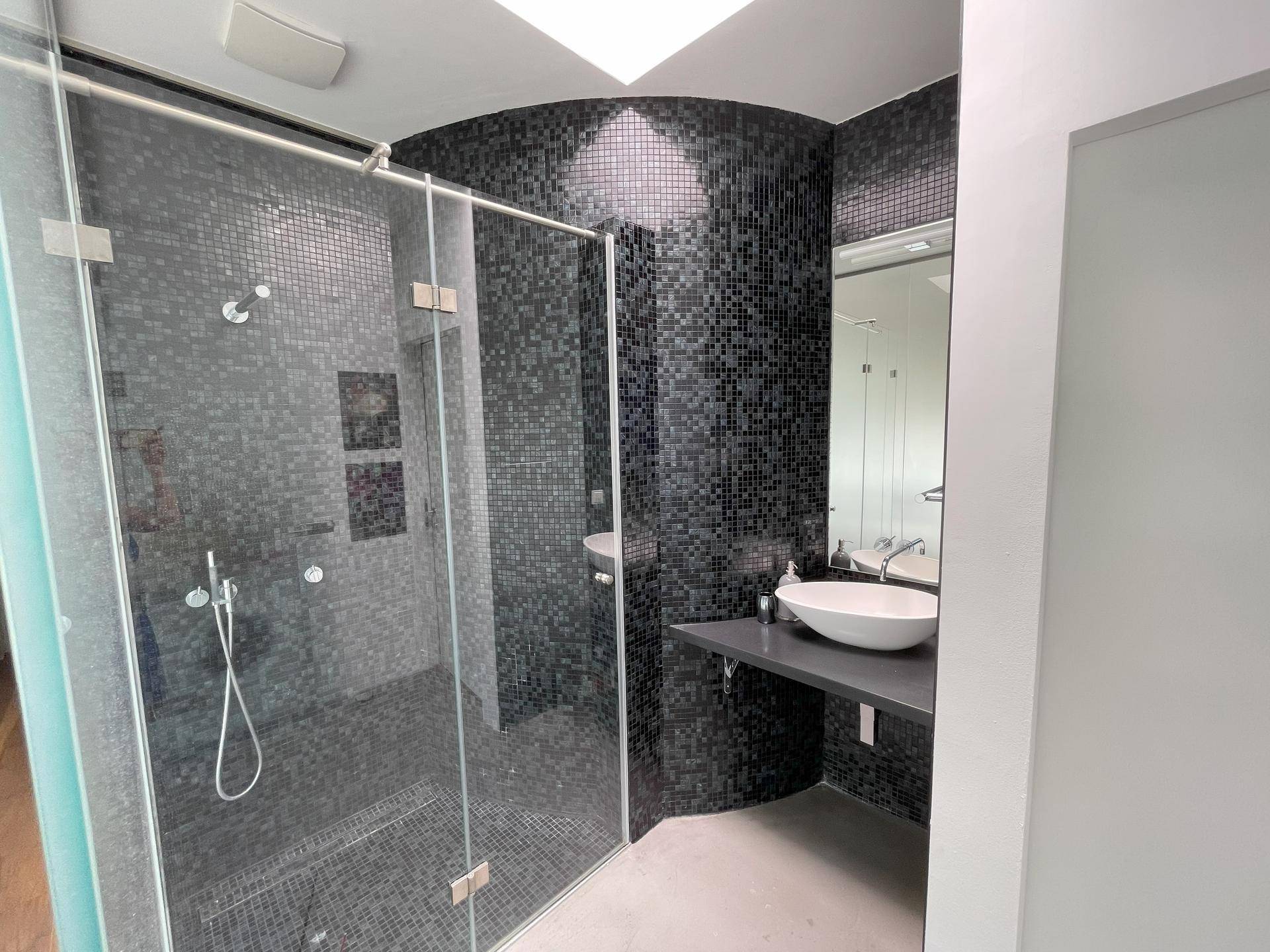 Modernes Badezimmer mit schwarzen Mosaikfliesen, begehbarer Dusche und Aufsatzwaschbecken.