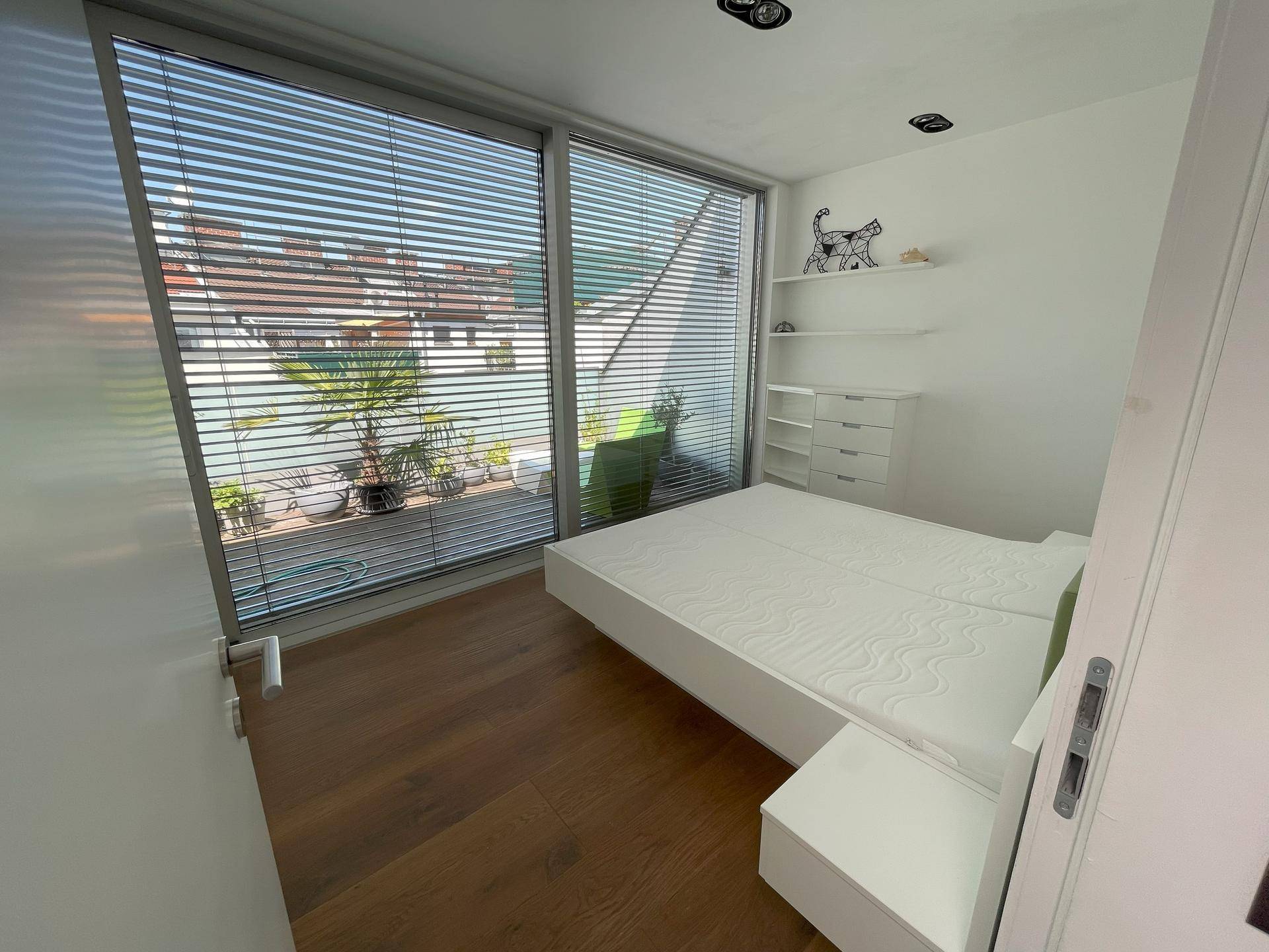 Helles Schlafzimmer mit großem Fenster, modernem Bett und Zugang zur Terrasse.