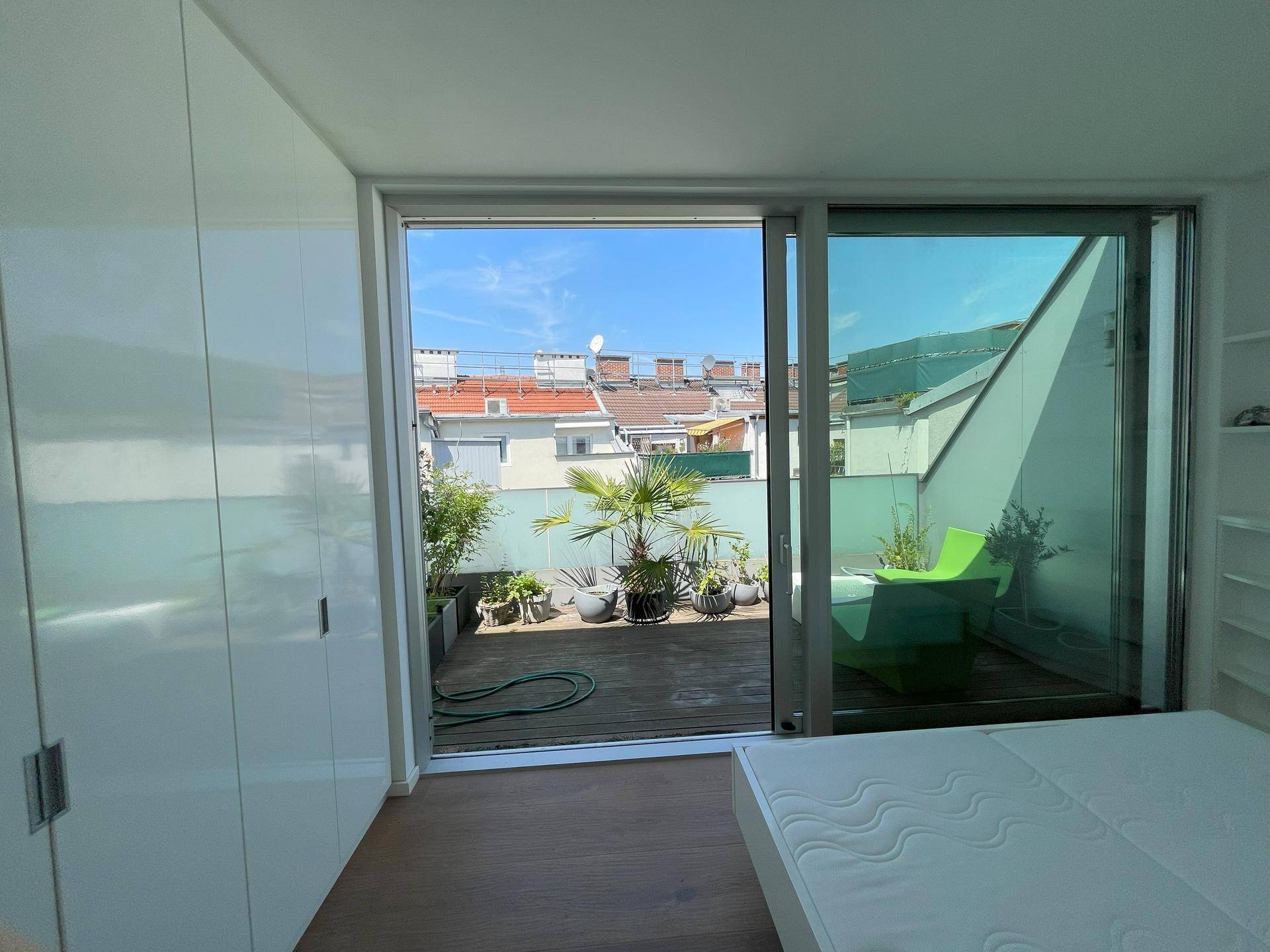 Schlafzimmer mit großer Glasschiebetür, die auf die begrünte Terrasse führt.