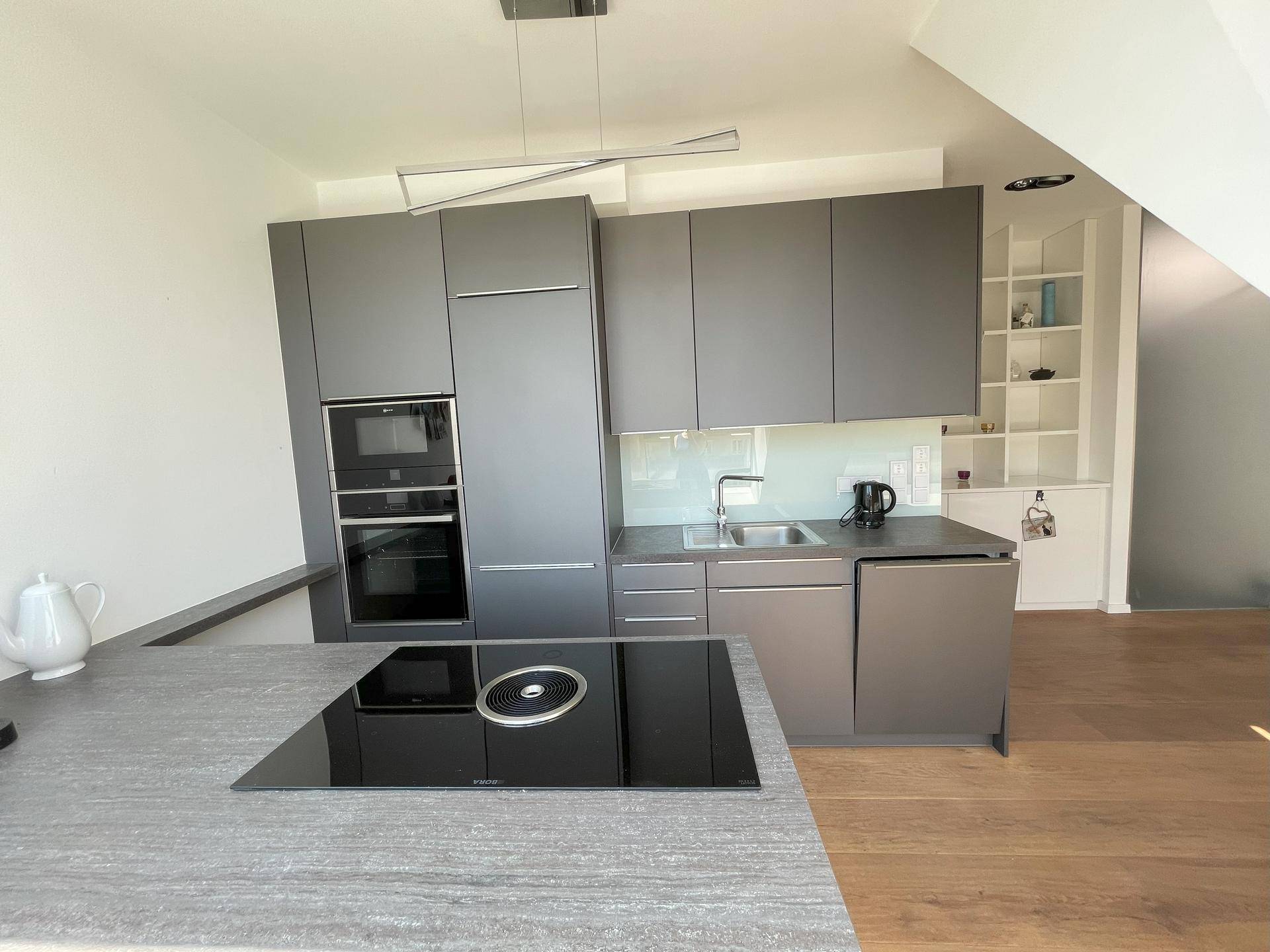 Moderne Küche mit Induktionskochfeld, Einbaugeräten und grauen Schränken.