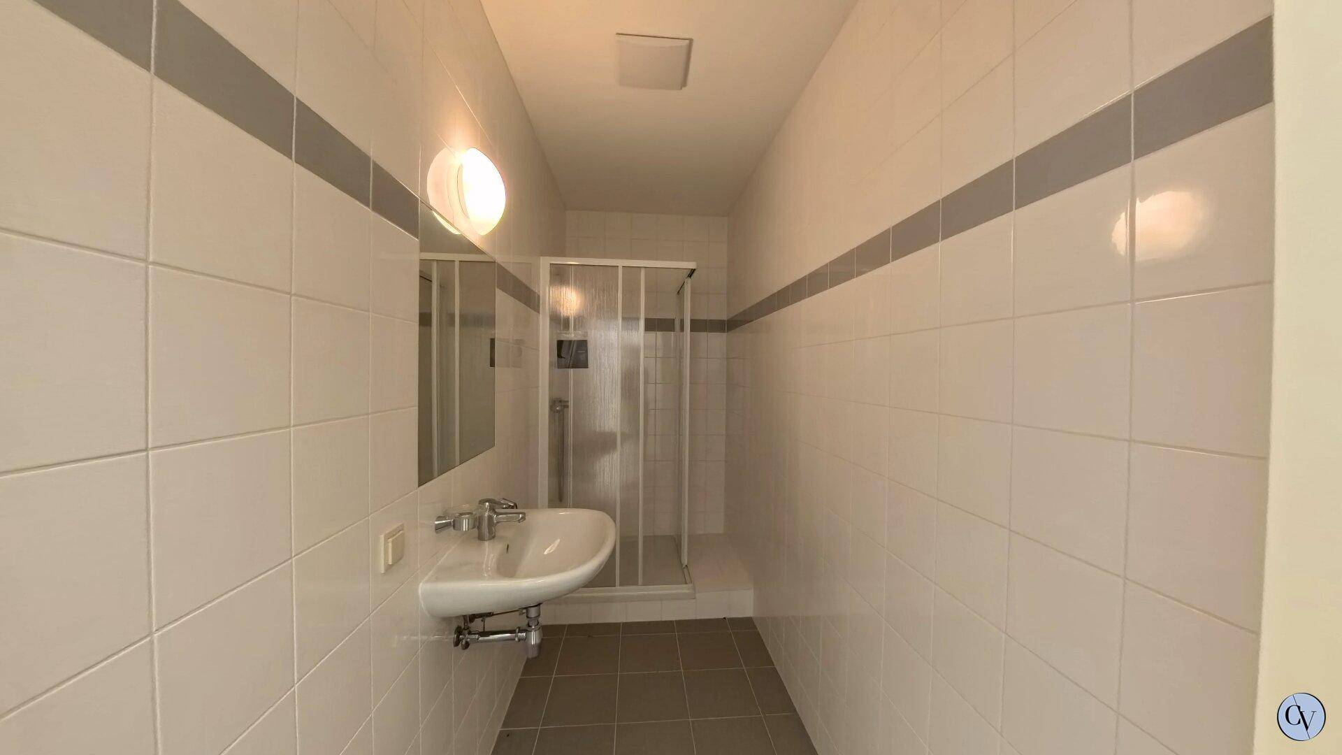 Gefliestes Badezimmer mit Duschkabine und Waschbecken, in einem sauberen und funktionalen Zustand.