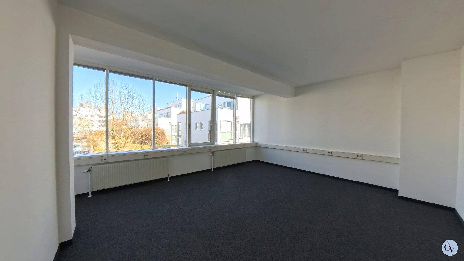 Heller Büroraum mit durchgehender Fensterfront, die für viel natürliches Licht und eine weite Aussicht sorgt.