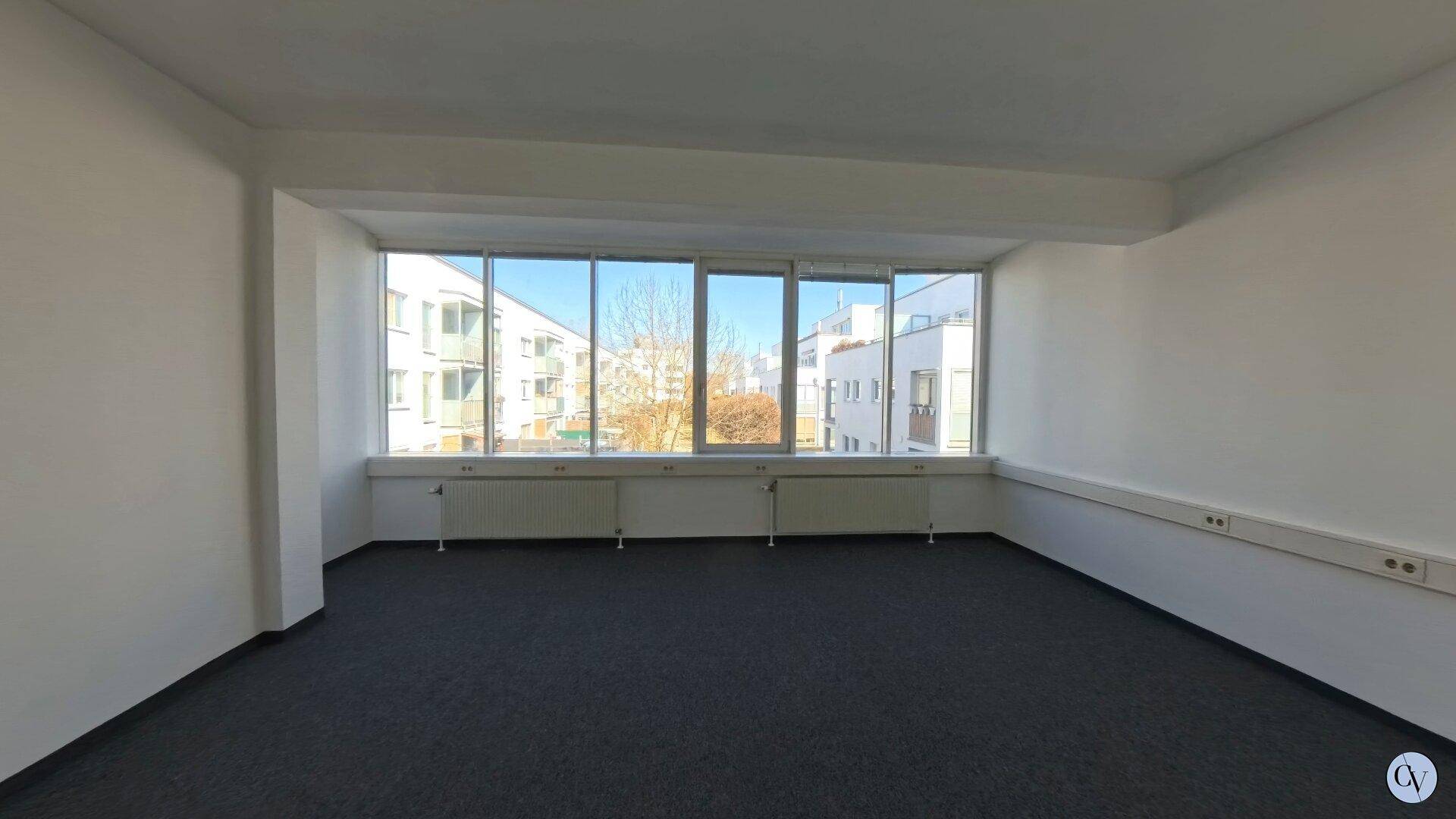 Geräumiger Büroraum mit breiter Fensterfront, die den Blick auf die umliegende Bebauung freigibt.
