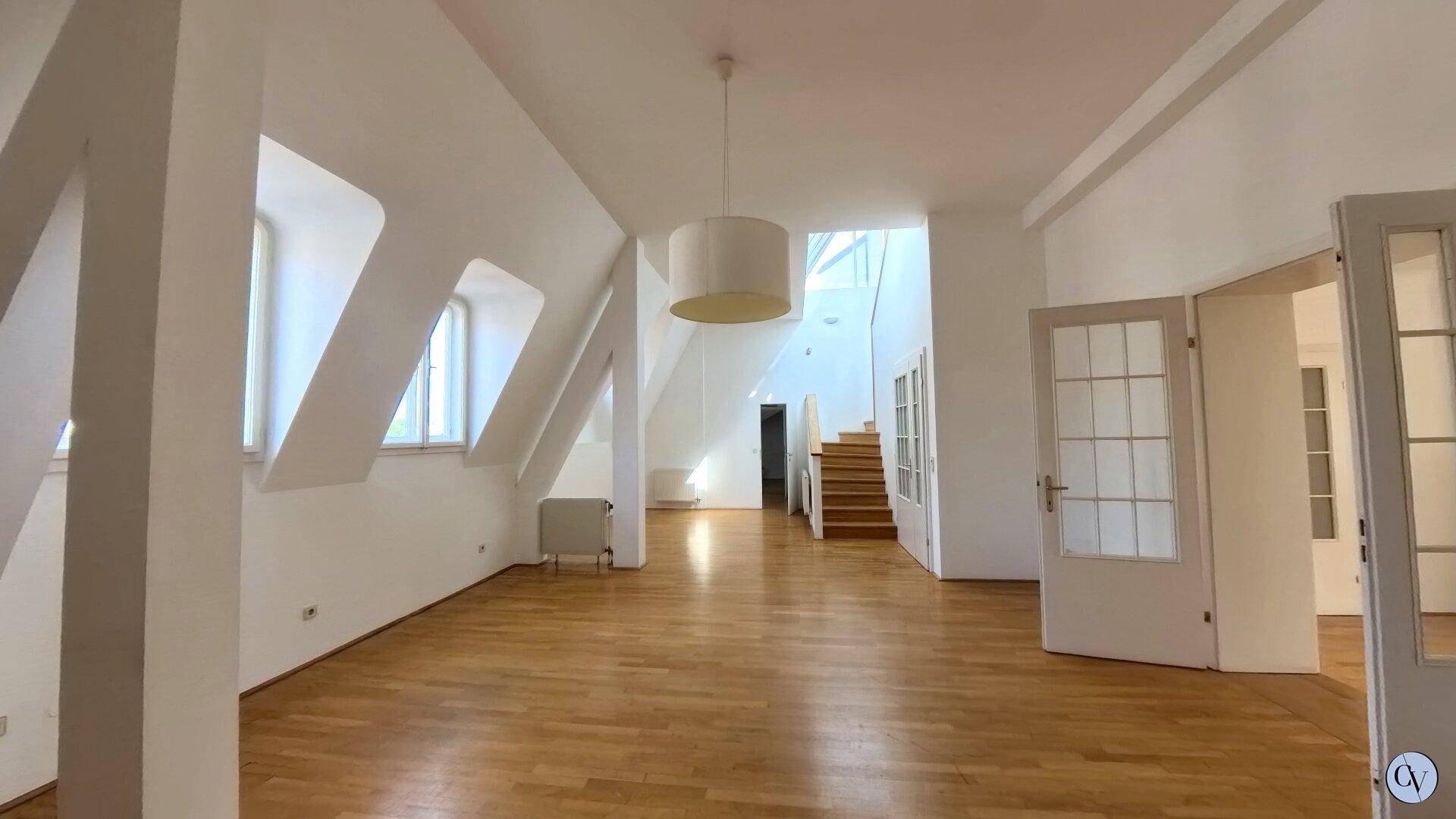 Helles, offenes Dachgeschosszimmer mit Holzparkettboden, sichtbarer Treppe und schrägen Wänden.