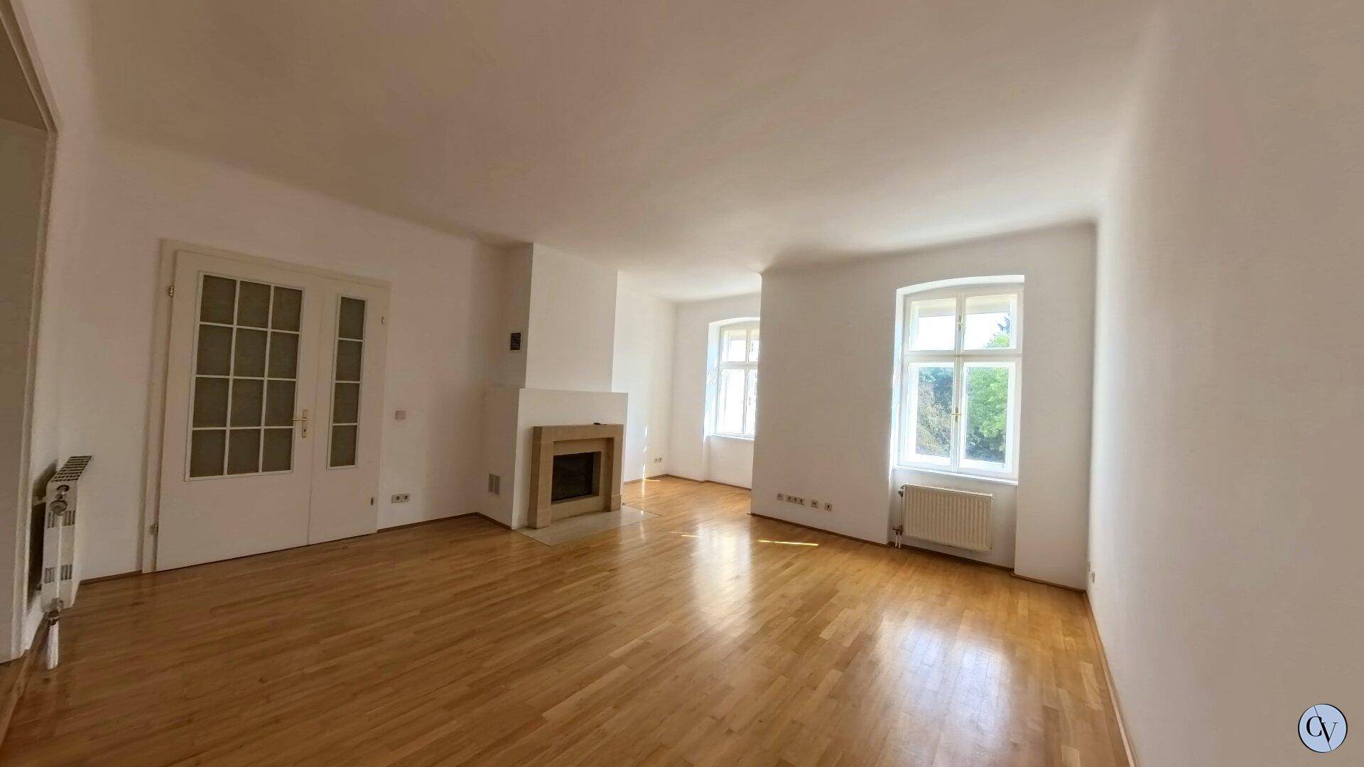 Helles Wohnzimmer mit Parkettboden, Kamin und Zugang zu weiteren Räumen.