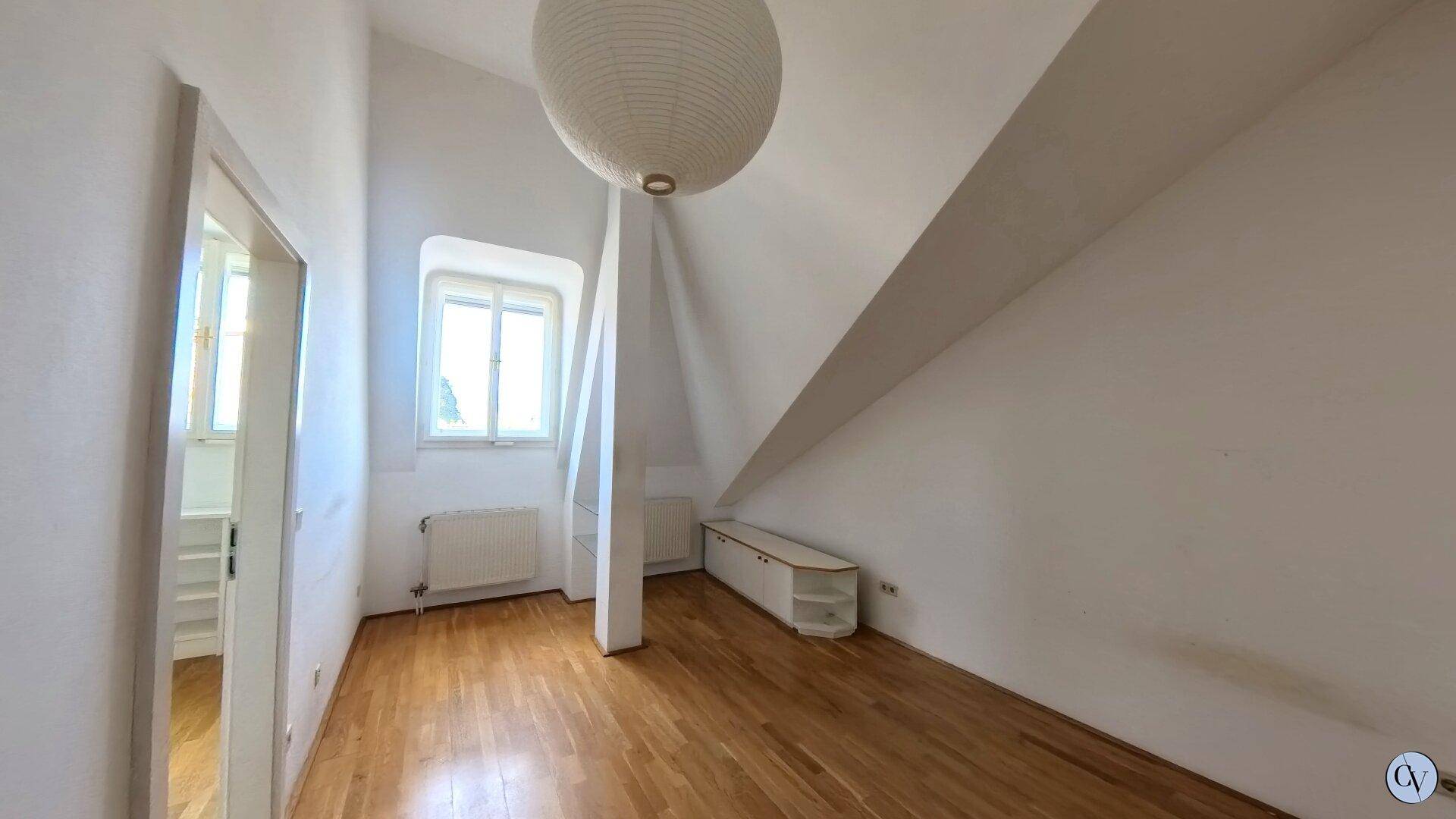 Gemütliches Schlafzimmer im Dachgeschoss mit Holzparkett, schräger Decke und Fenster.