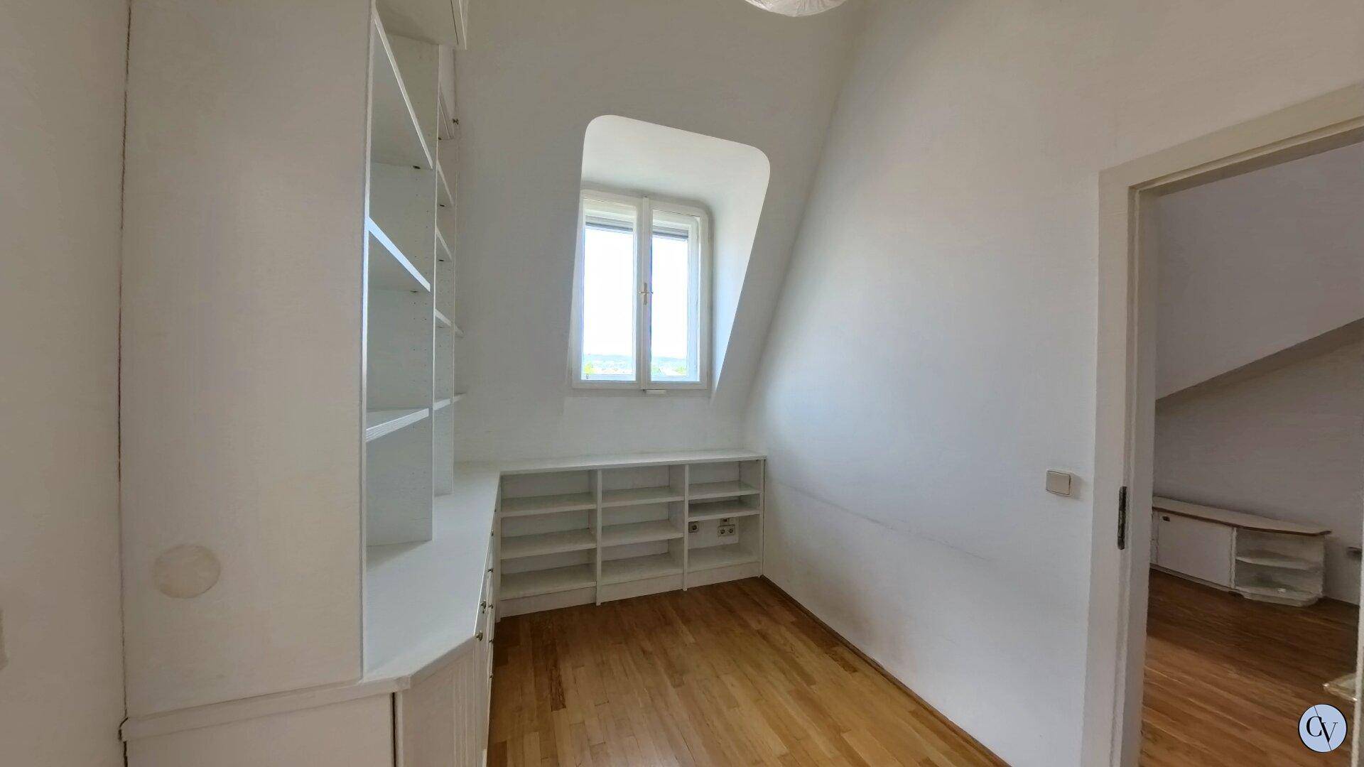 Heller Raum im Dachgeschoss mit Einbauregalen, Holzparkett und schräger Decke.