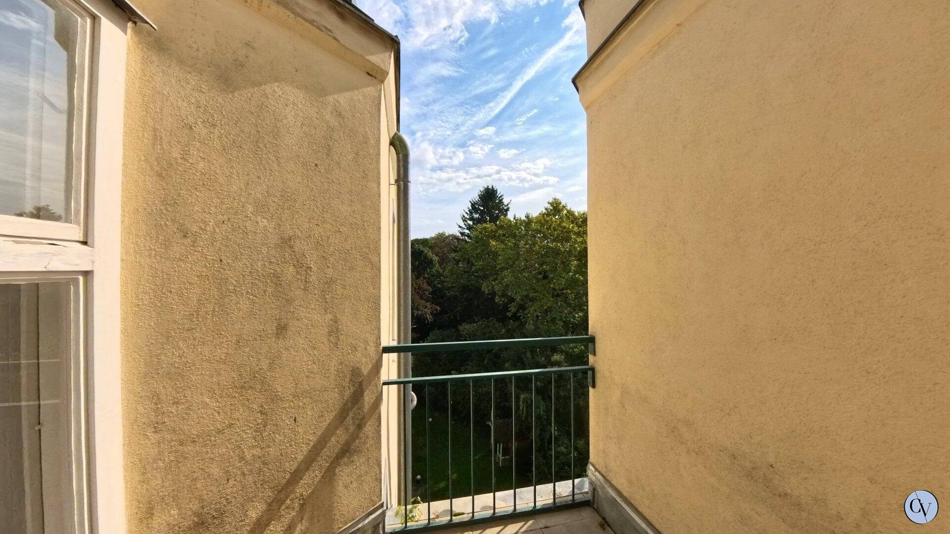 Kleiner Balkon mit Blick ins Grüne und traditionellem Geländer zwischen zwei Gebäudeteilen.