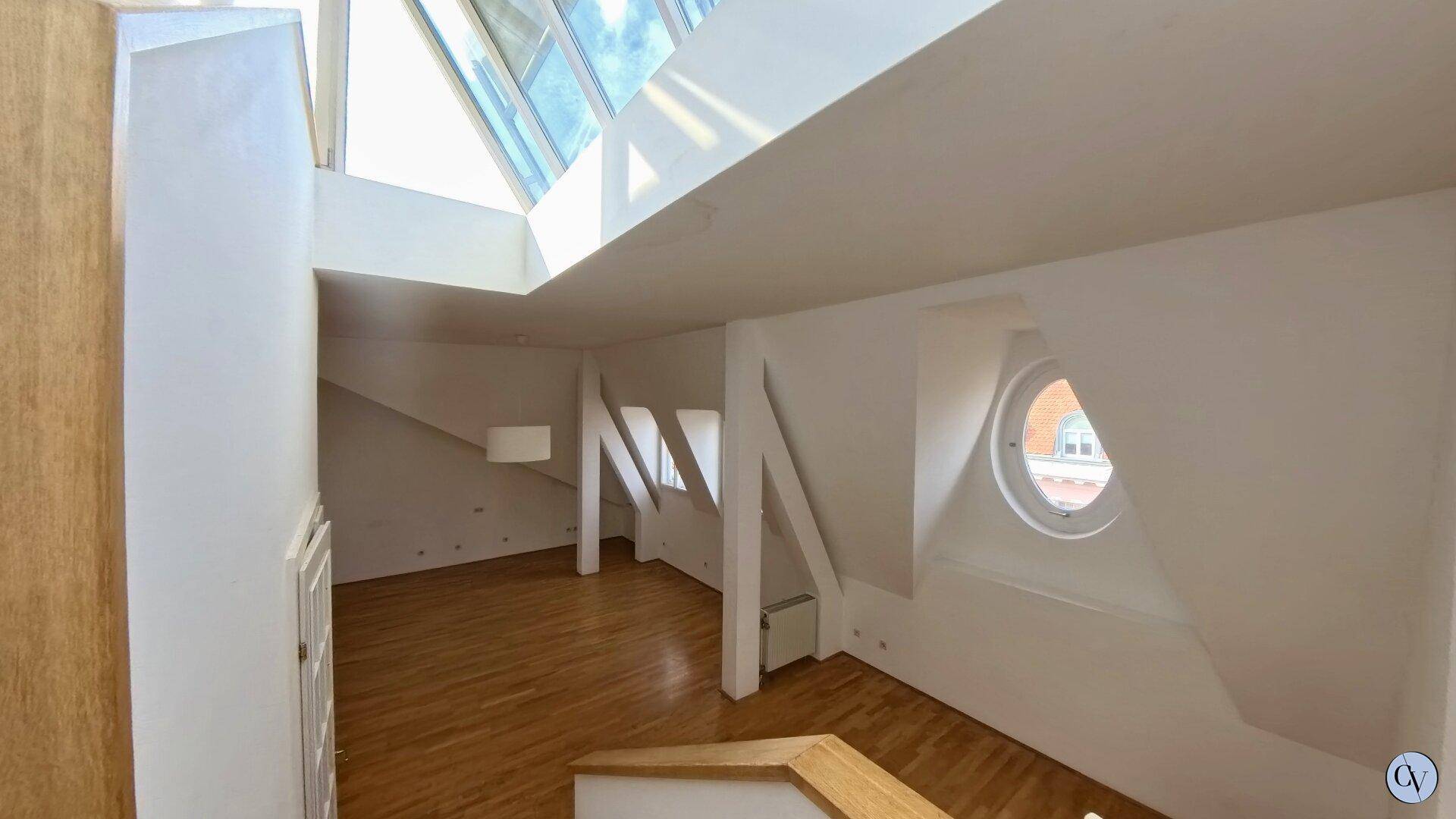 Lichtdurchfluteter Dachgeschossbereich mit Holzparkett, runden Fenstern und großem Oberlicht.