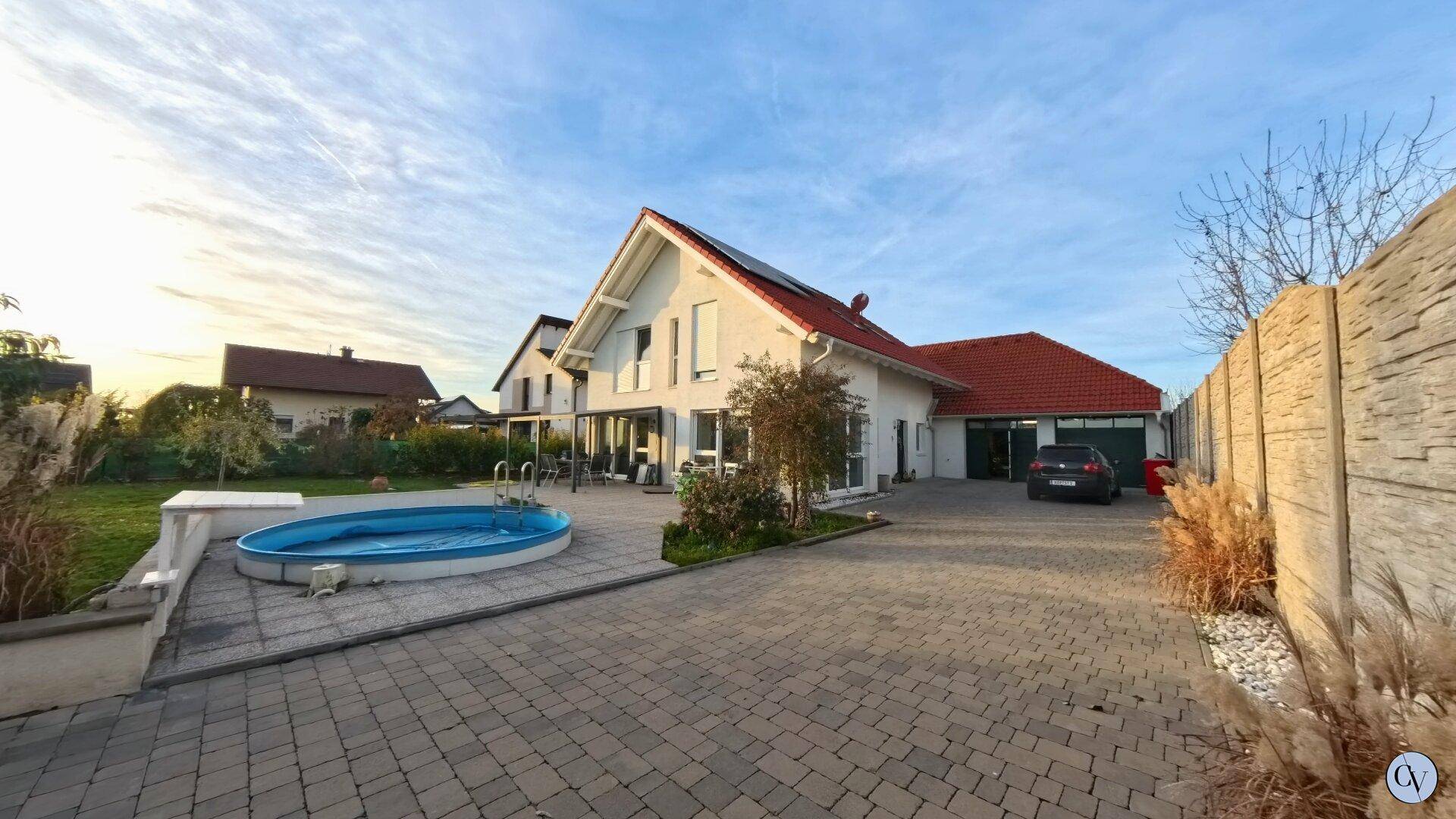 Einfamilienhaus mit gepflasterter Auffahrt, Garage und einem kleinen Aufstellpool im Garten.