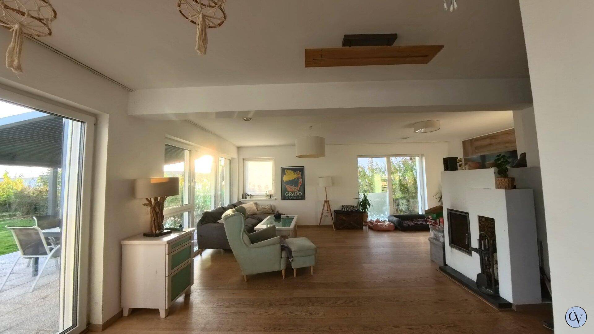 Geräumiges Wohnzimmer mit Holzboden, Kamin und Zugang zur Terrasse durch große Fenster.