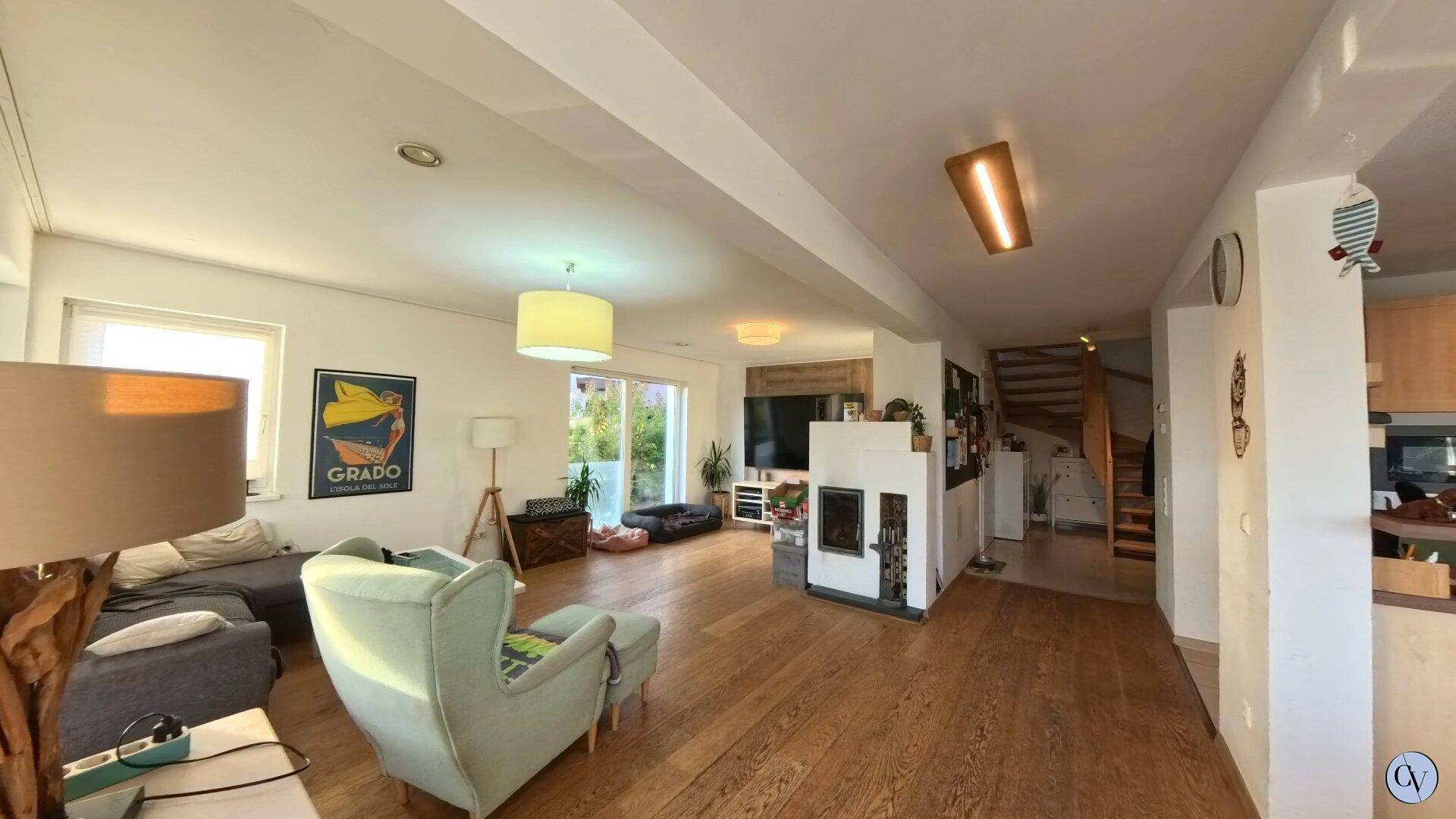 Helles Wohnzimmer mit Kamin, Holzboden und offenem Übergang zum Treppenbereich.