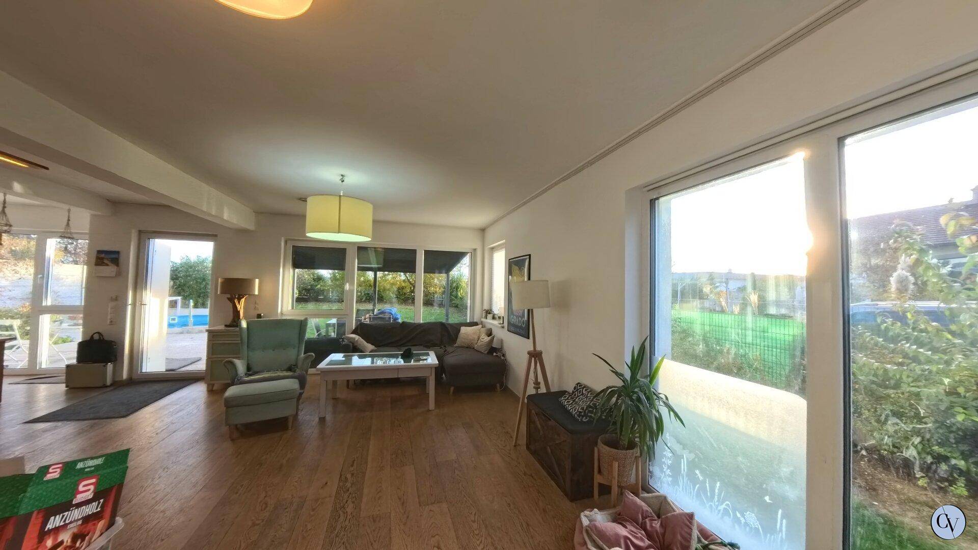 Lichtdurchflutetes Wohnzimmer mit großen Fenstern, Holzboden und Blick ins Grüne.