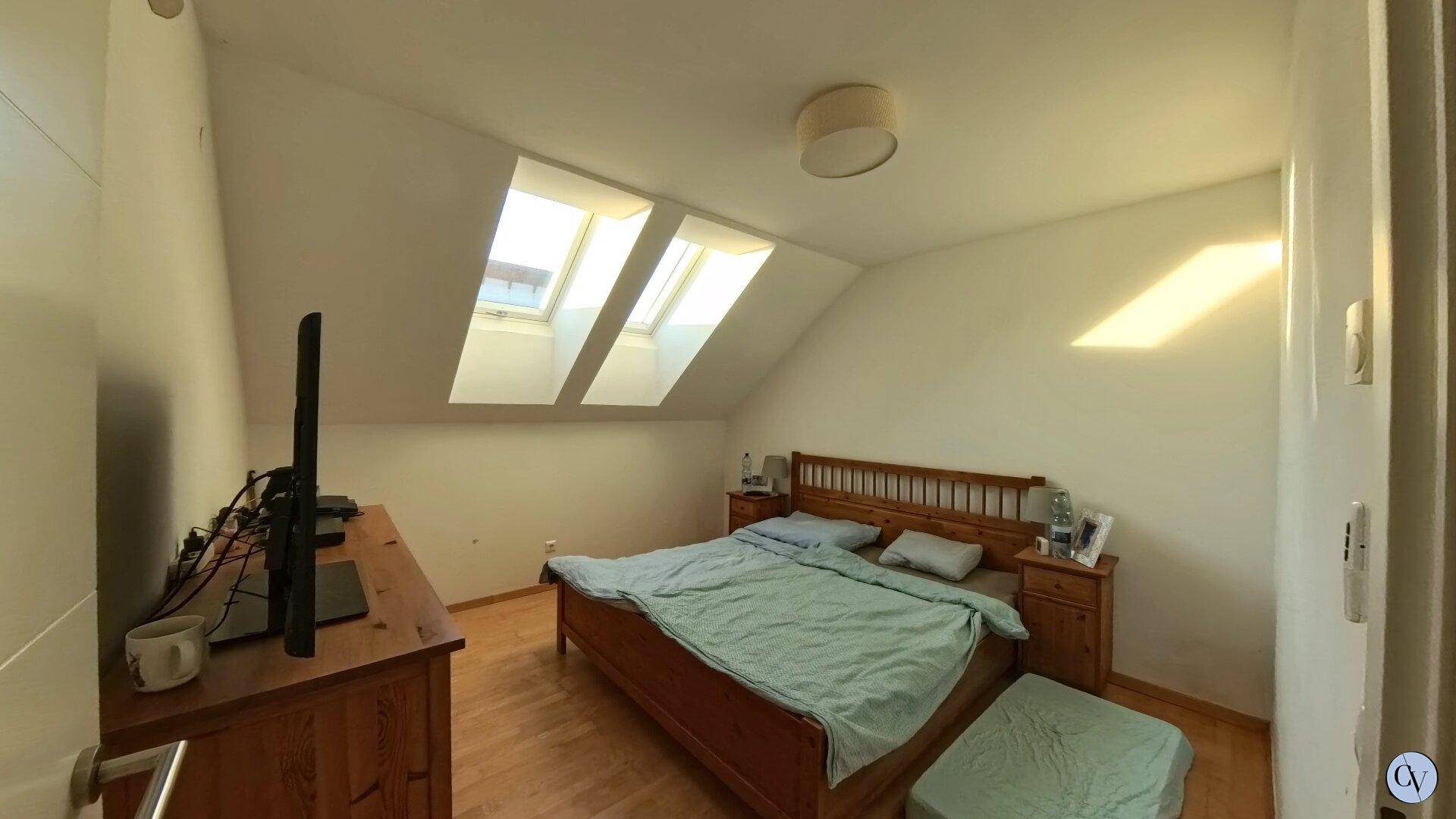 Helles Schlafzimmer mit Holzbett, Kommode und zwei Dachfenstern für viel Tageslicht.