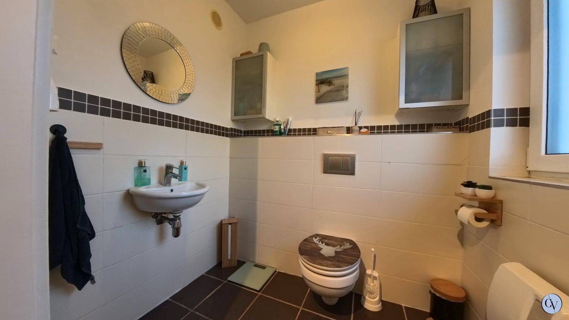 Gäste-WC mit modernem Waschbecken, Wand-WC und Fenster für natürliche Belüftung.