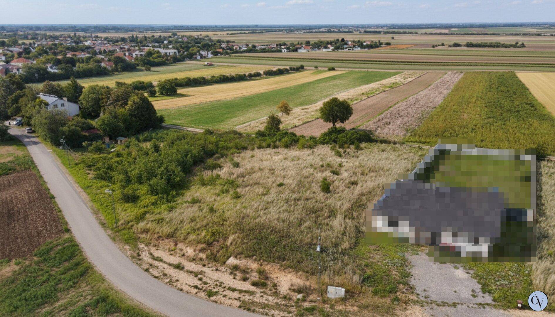 Übersicht des Grundstücks mit angrenzenden Feldern und einem Dorf am Horizont unter blauem Himmel.