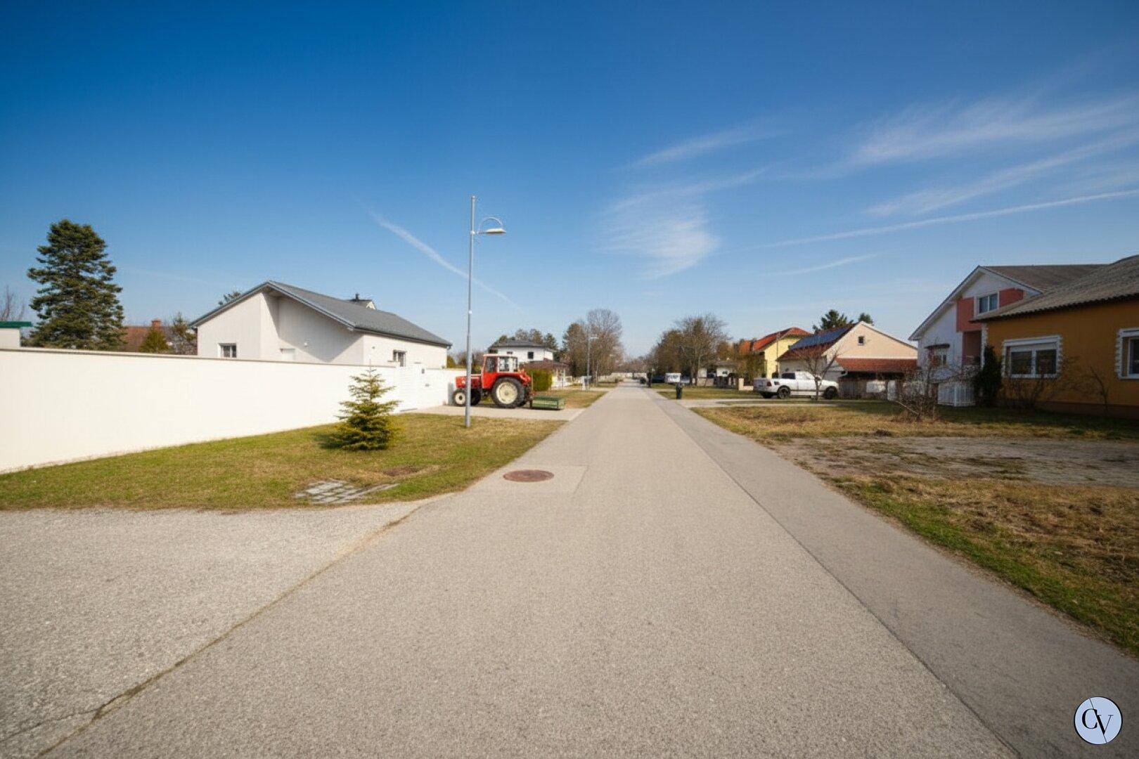 Ruhige Wohnstraße mit Einfamilienhäusern und einem Traktor am Straßenrand unter blauem Himmel.