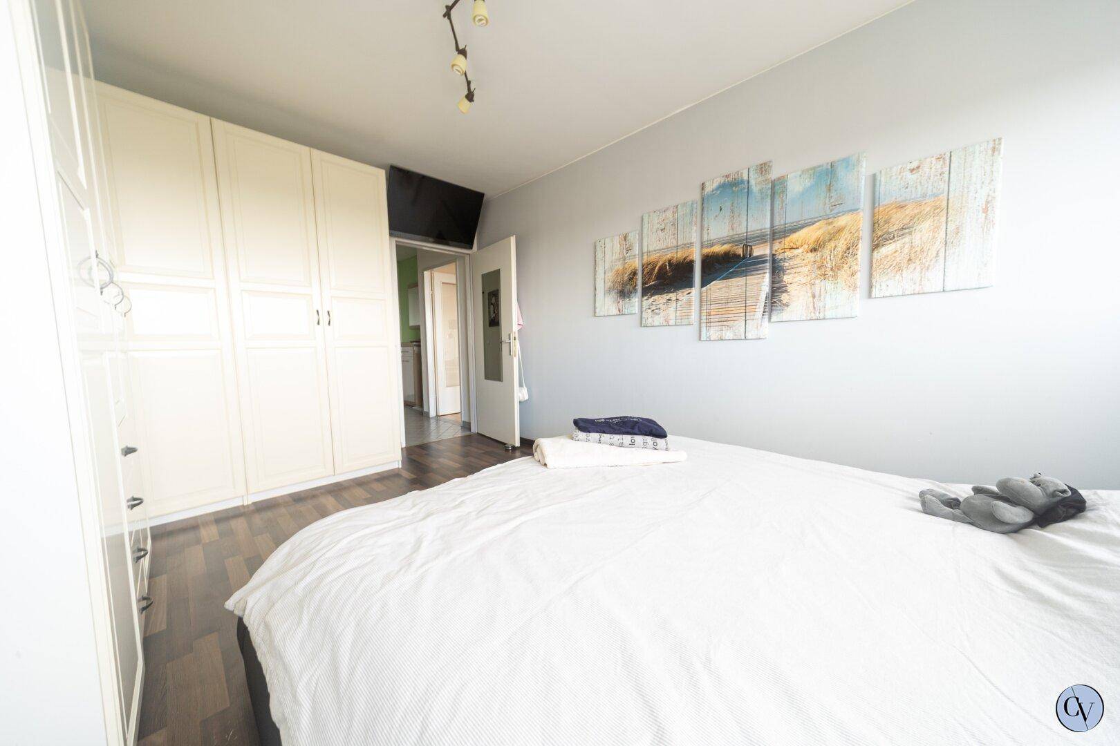 Helles Schlafzimmer mit Laminatboden, weißem Kleiderschrank und Wanddekoration.