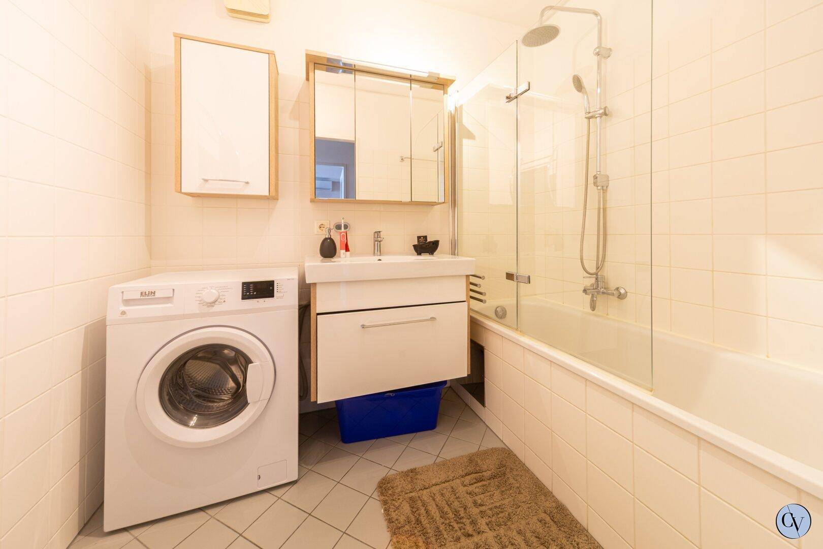 Badezimmer mit Badewanne, Duschfunktion, Waschmaschine und hellen Fliesen.