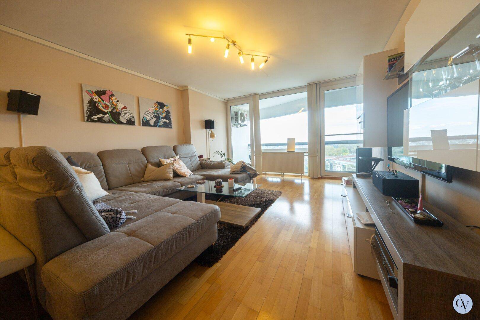Gemütliches Wohnzimmer mit großem Sofa, Holzboden und Zugang zum Balkon.
