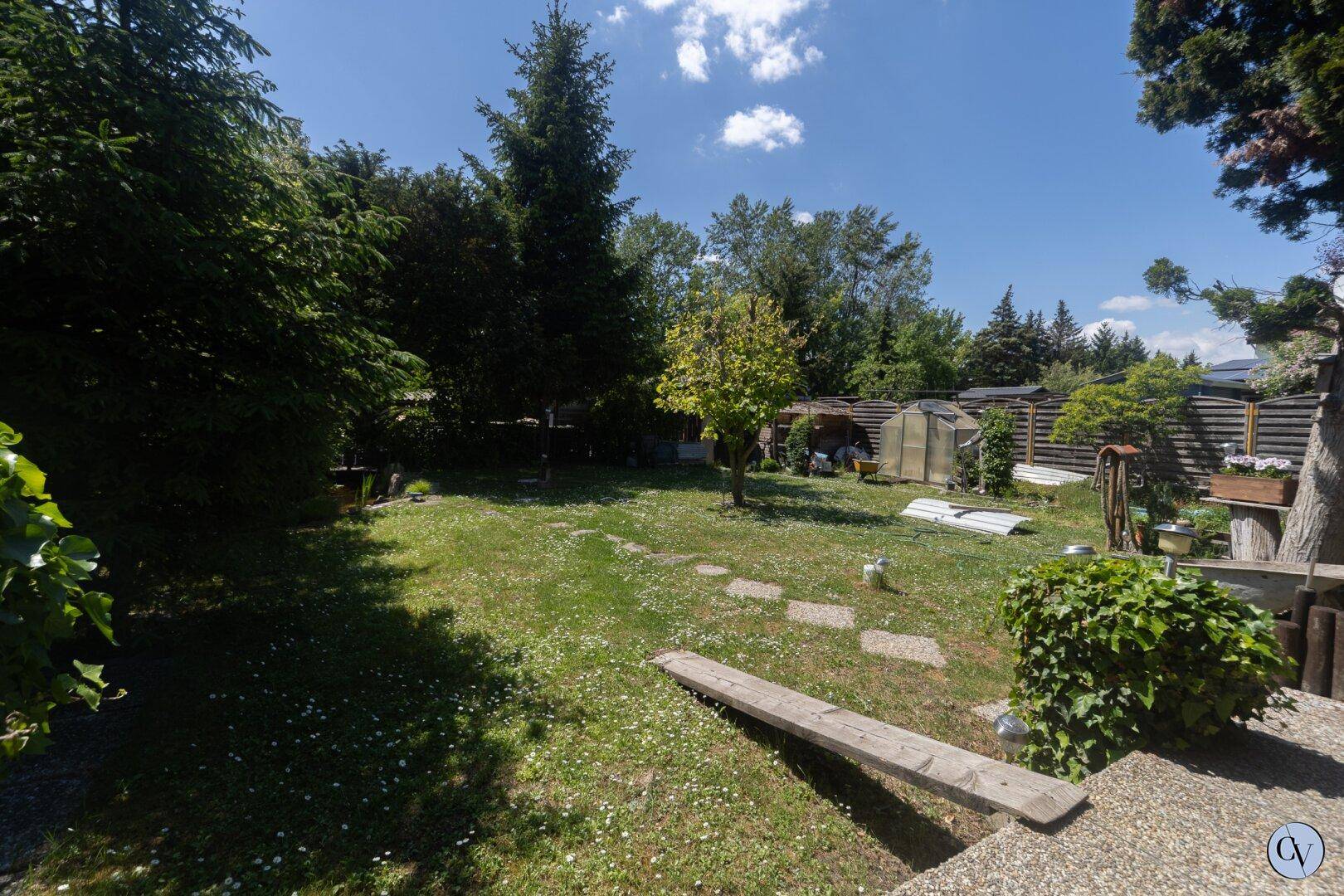 Gepflegter Garten mit weitläufiger Rasenfläche, Bäumen und Trittsteinen unter blauem Himmel.