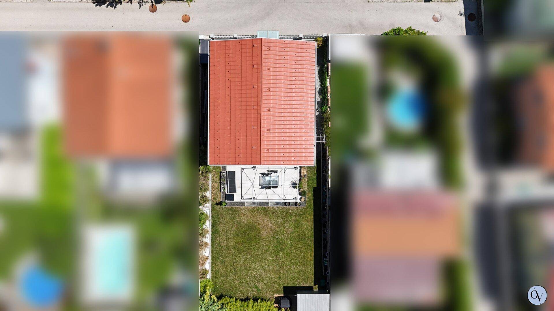 Luftaufnahme eines Hauses mit rotem Ziegeldach, möblierter Terrasse und gepflegtem Rasenbereich.