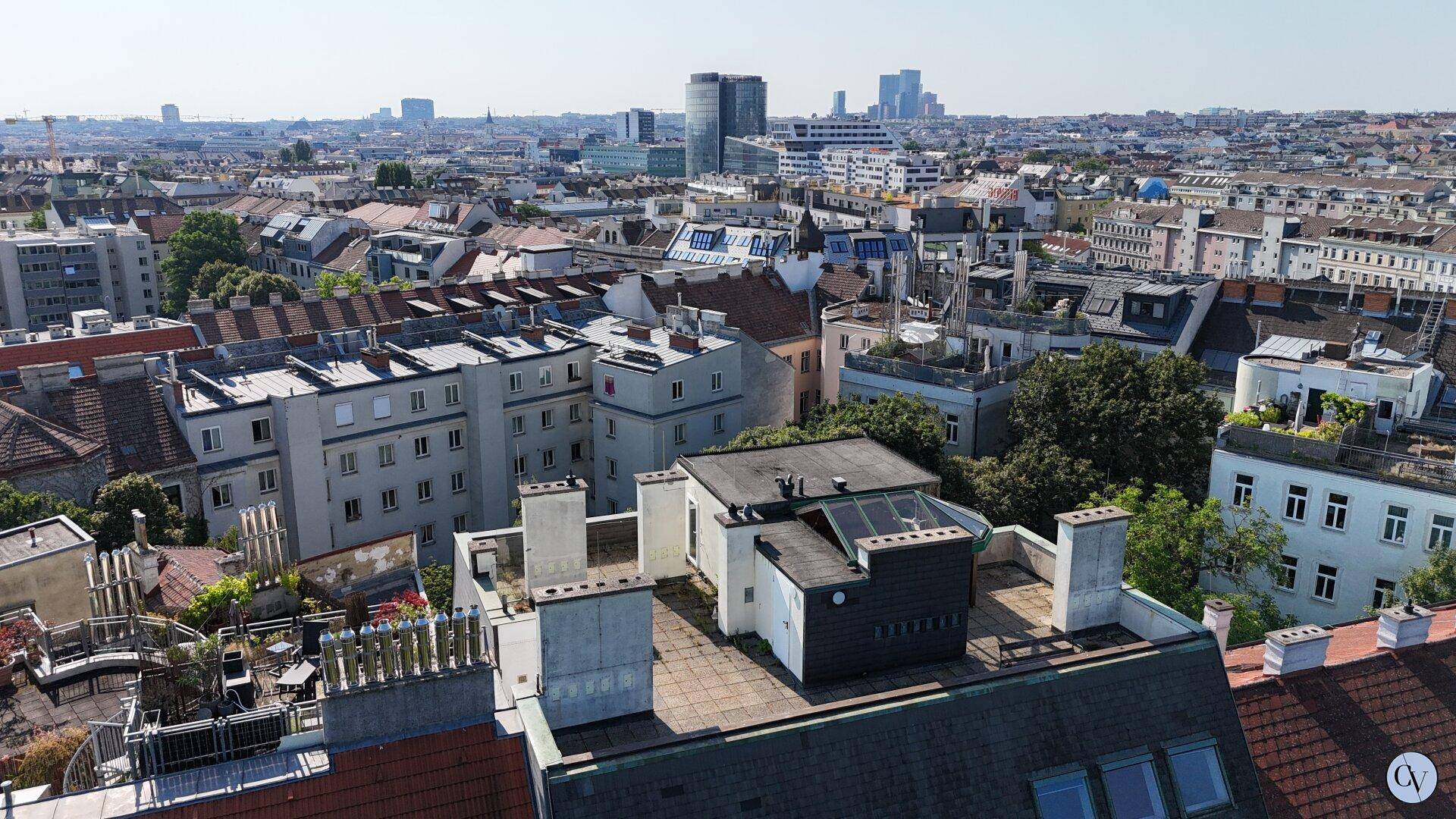 Panoramablick über die Dächer einer Stadt mit urbaner Skyline im Hintergrund.