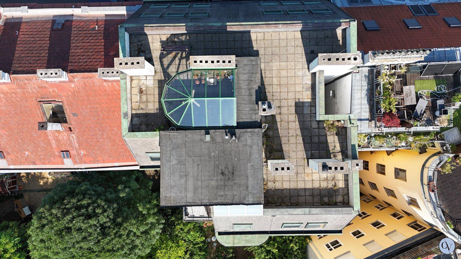 Luftaufnahme von Dächern mit verschiedenen Dachformen und einer verglasten Kuppel.