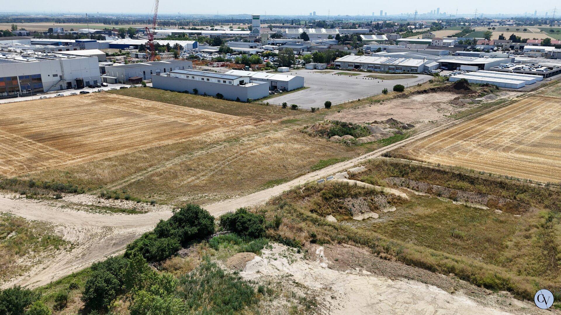 Luftaufnahme eines Industriegebiets mit angrenzenden Feldern und einer erkennbaren Stadtkulisse in der Ferne.