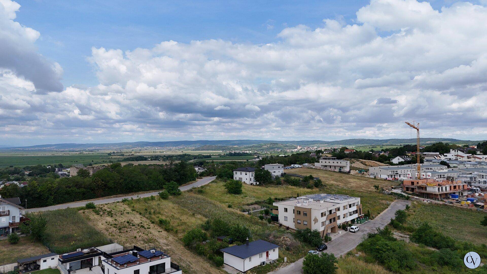 Weitläufige Luftaufnahme einer Wohnsiedlung im Bau mit grünen Hügeln und weitem Blick.
