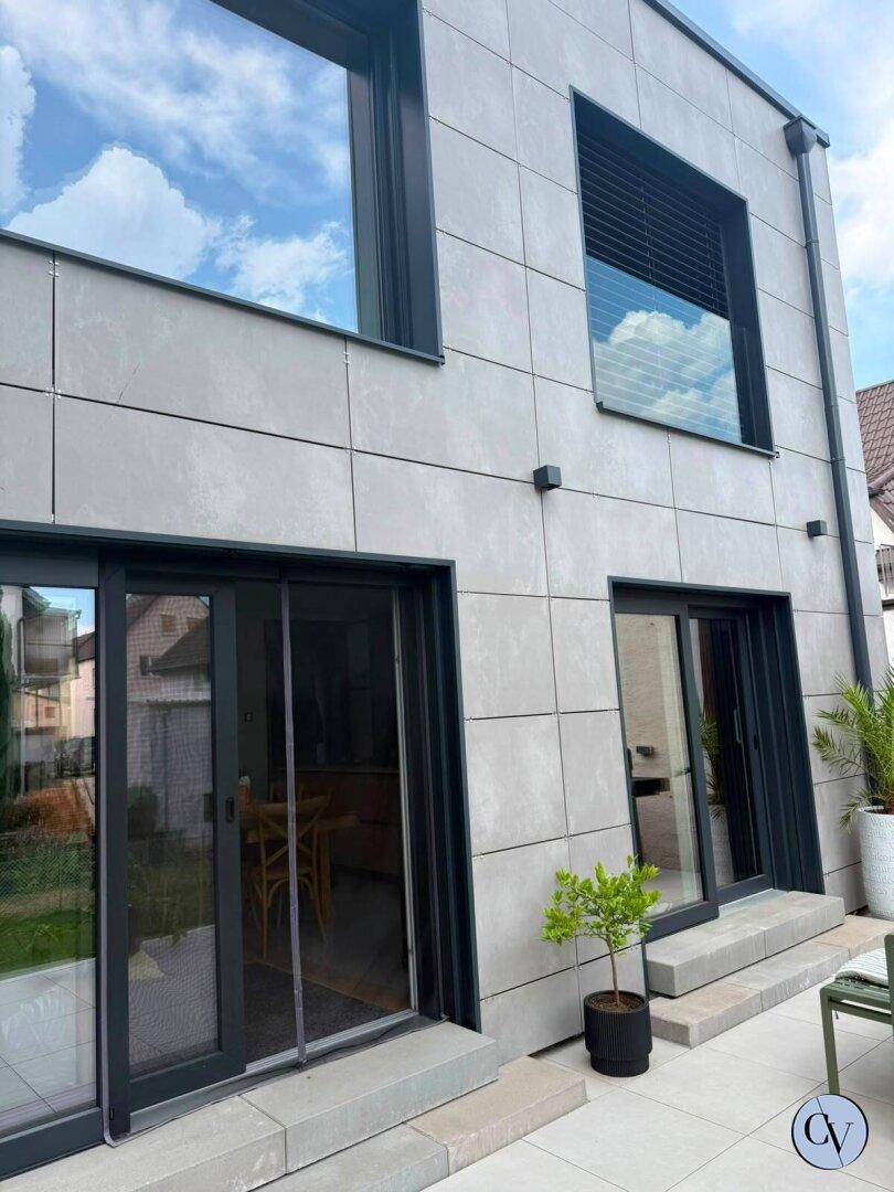 Nahaufnahme der modernen Hausfassade mit großen Schiebetüren und einer gepflasterten Terrasse.