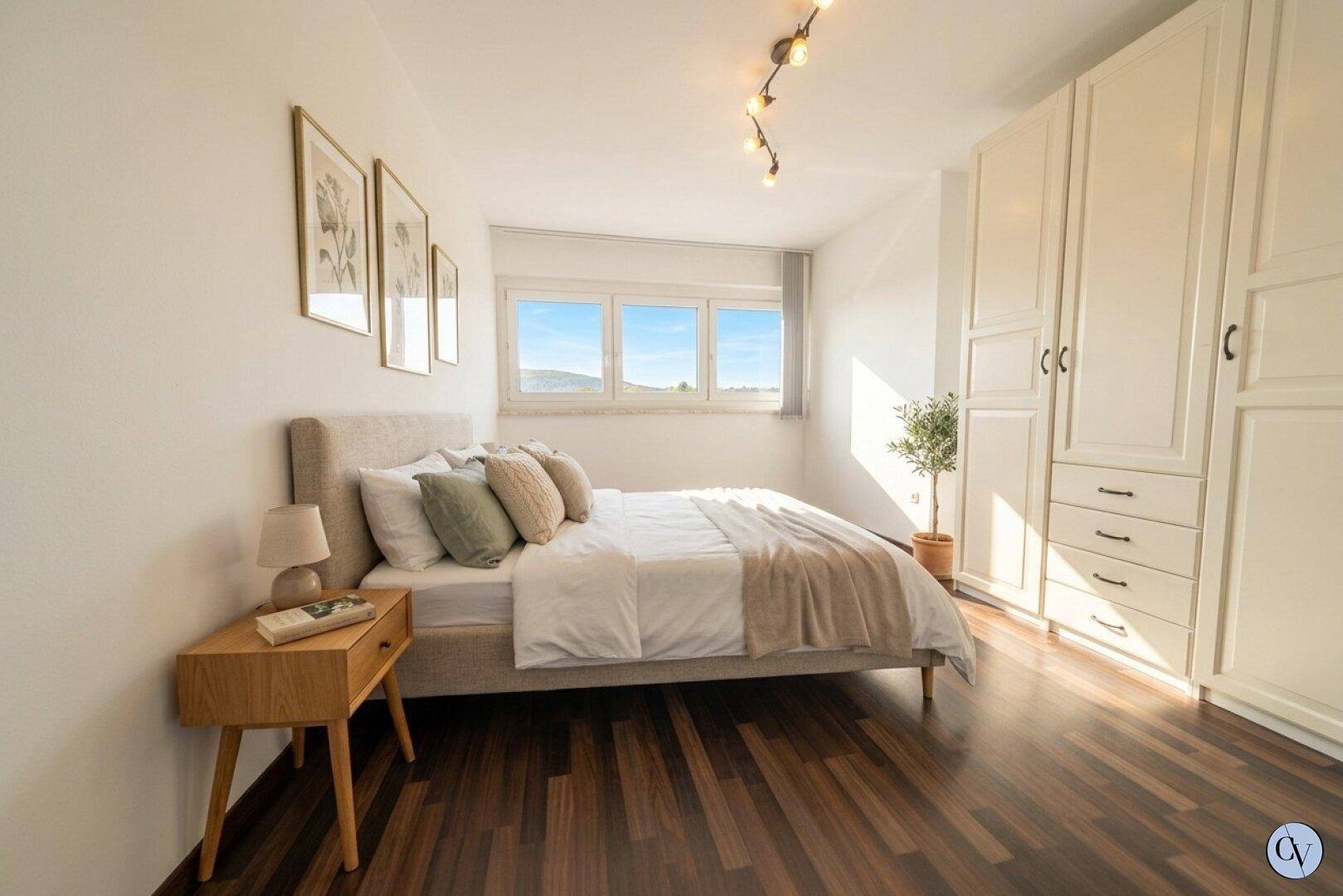 Helles Schlafzimmer mit Holzboden, Einbauschränken und Fenster mit Blick ins Grüne.