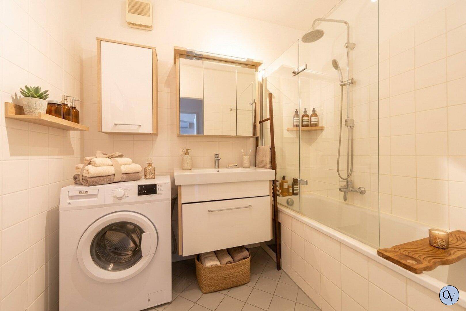 Modernes Badezimmer mit Badewanne, Dusche, Waschmaschine und hellen Fliesen.