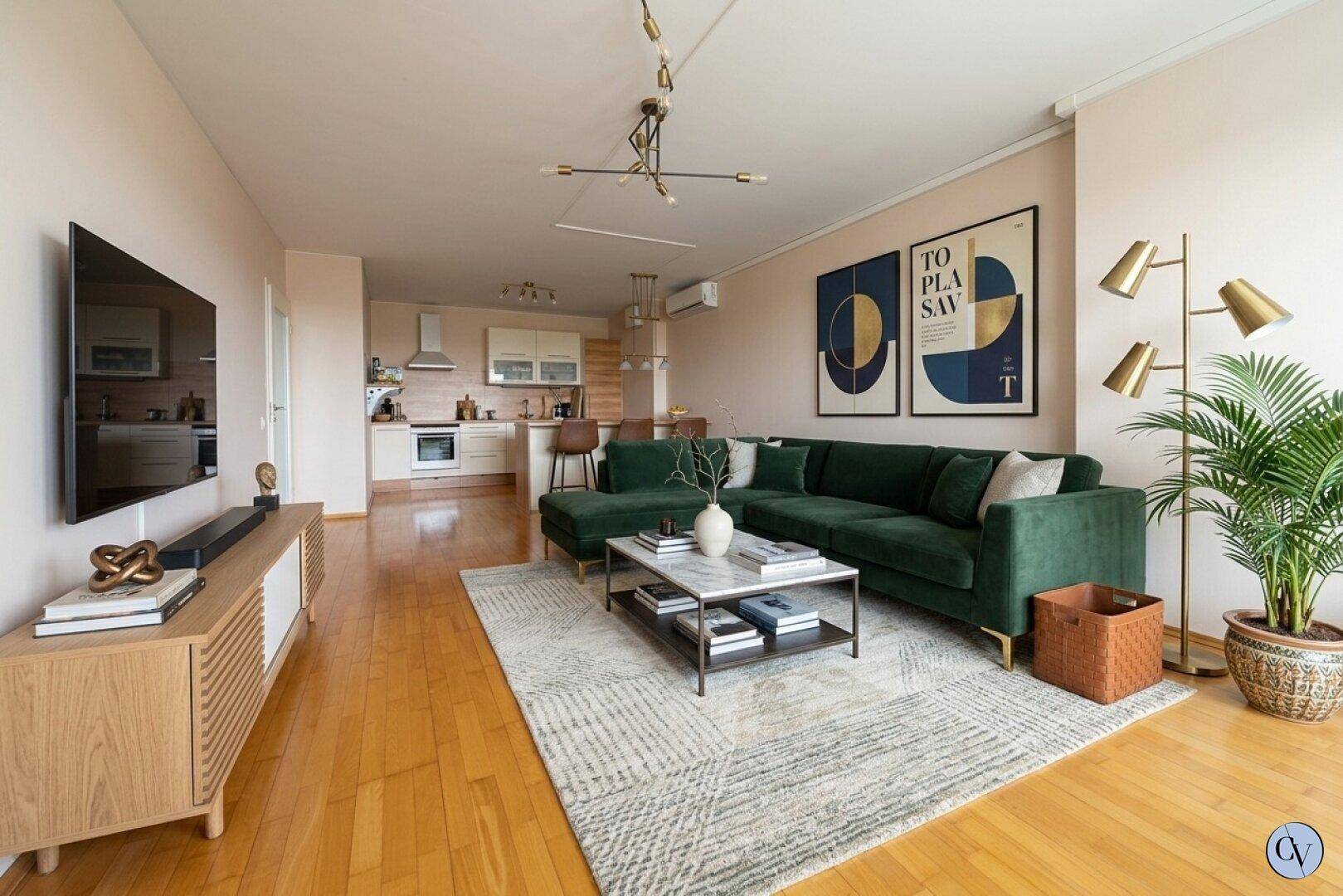 Offener Wohn- und Essbereich mit dunkelgrünem Sofa, Holzboden und integrierter Küche.