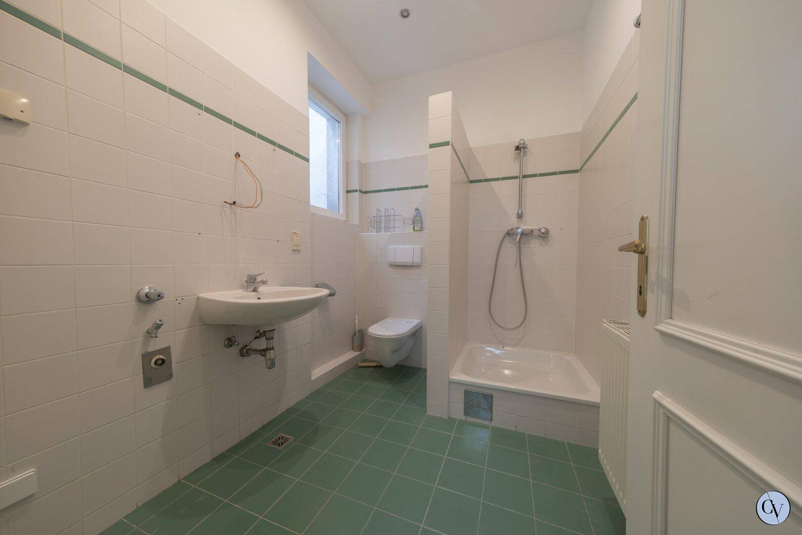 Badezimmer mit grünen Fliesen, Dusche, Waschbecken und Fenster.