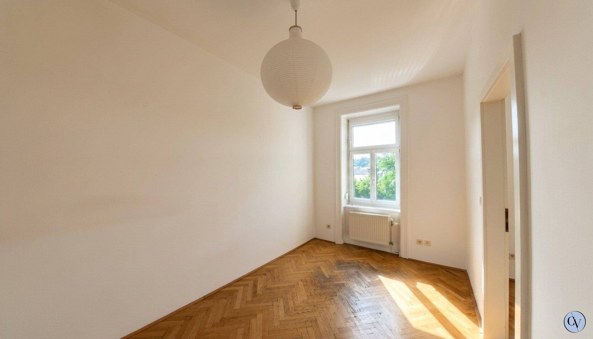 Helles Schlafzimmer mit Fischgrätparkett, Fenster und viel Tageslicht.